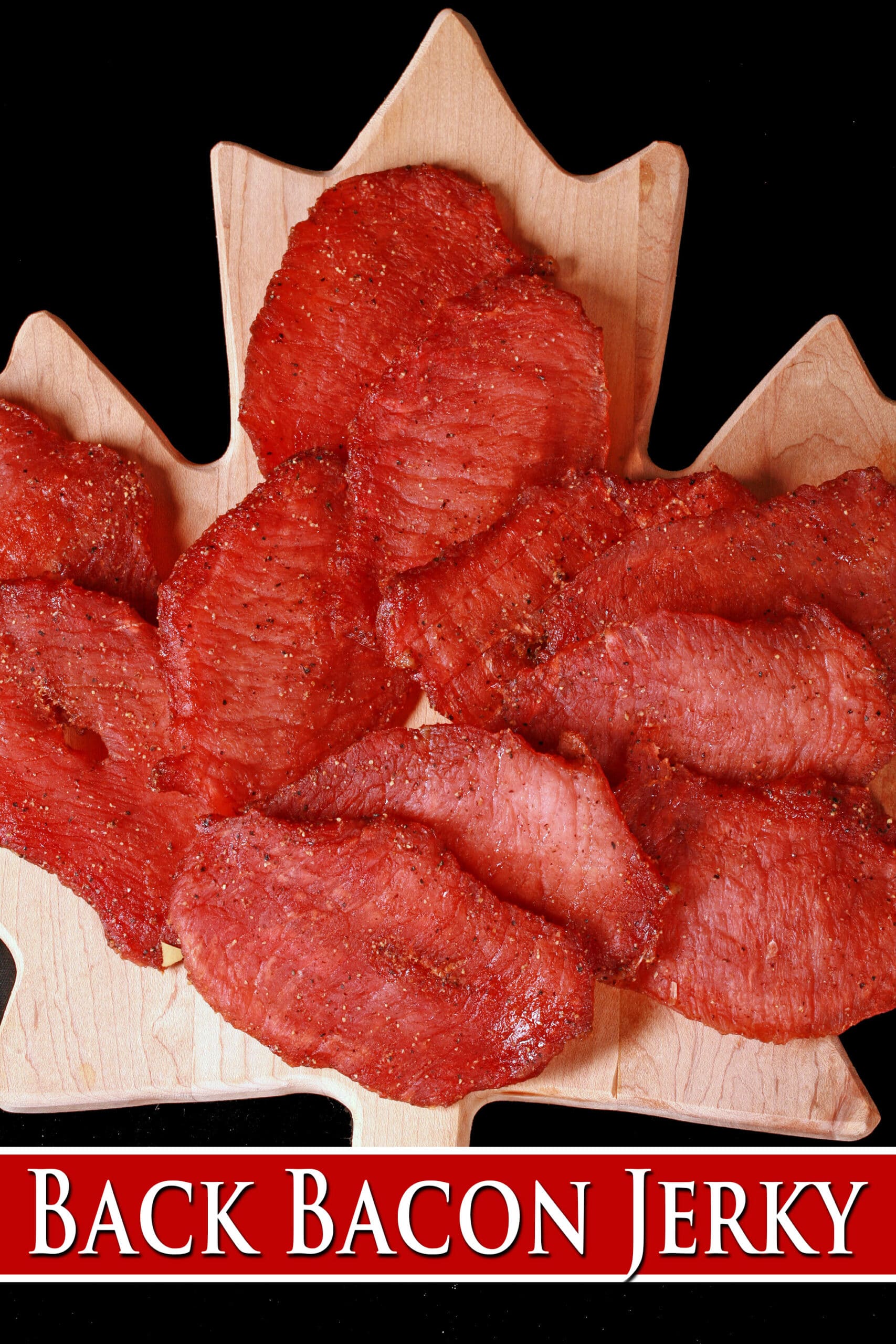 A pile of pink pork jerky slices on a maple leaf cutting board. Overlaid text says back bacon jerky.