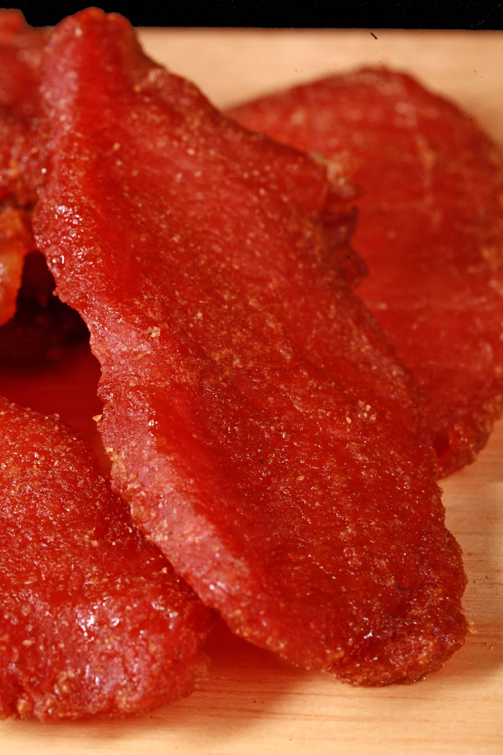 A pile of pork loin jerky slices on a wooden cutting board.