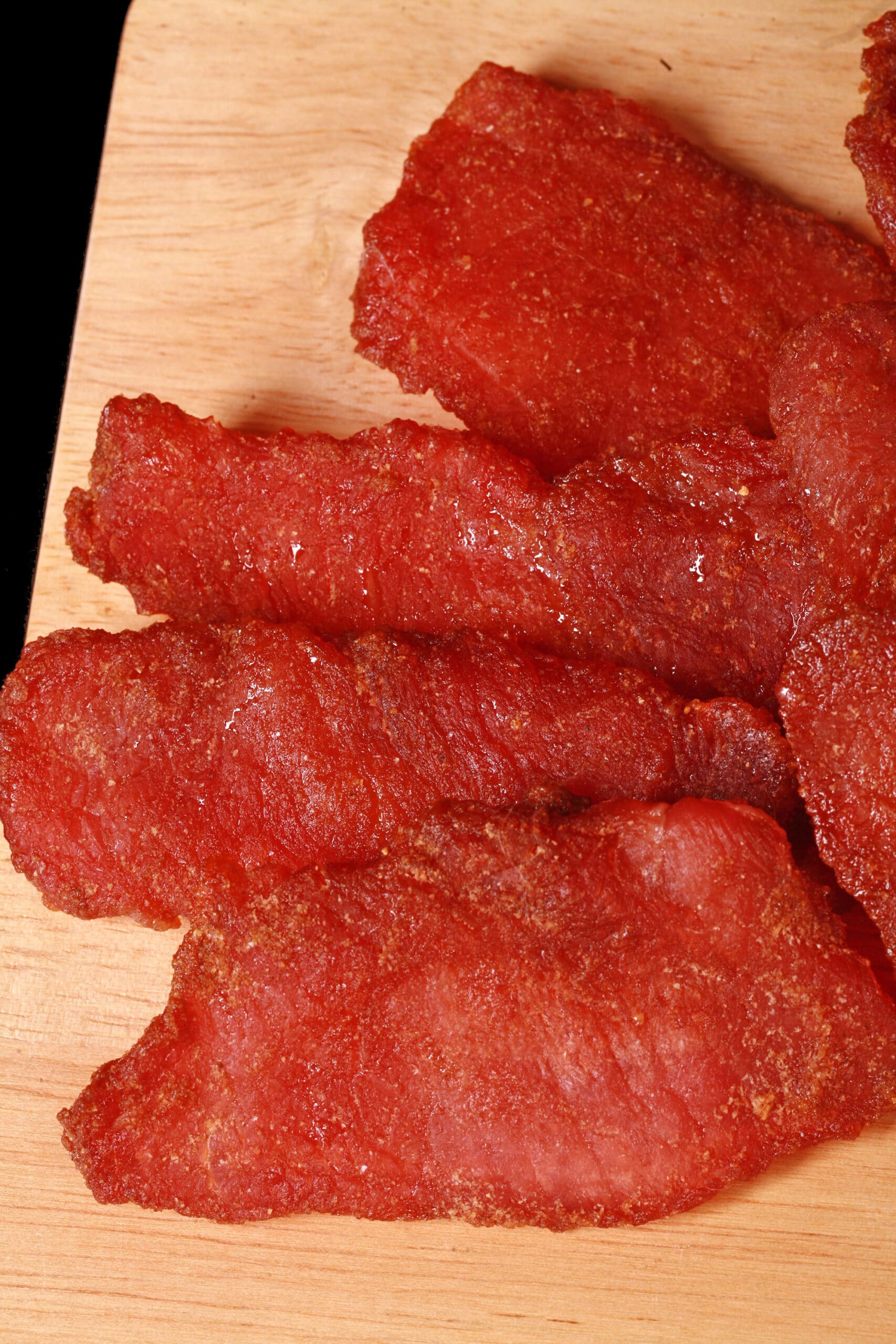 A pile of pork jerky slices on a wooden cutting board.