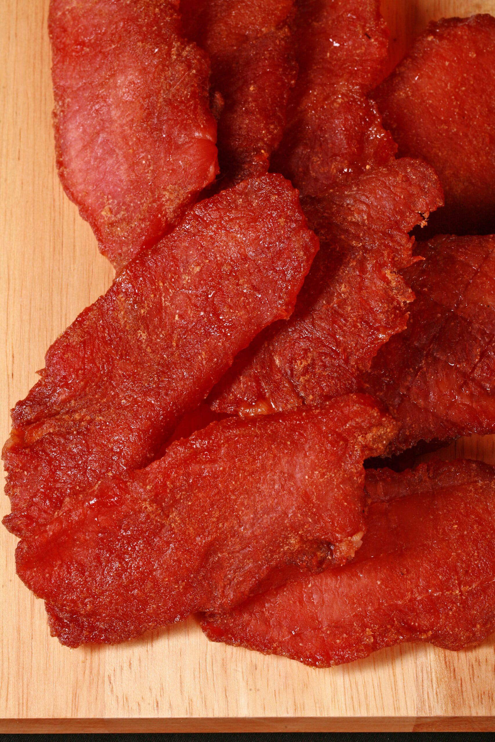 A pile of pork loin jerky slices on a wooden cutting board.