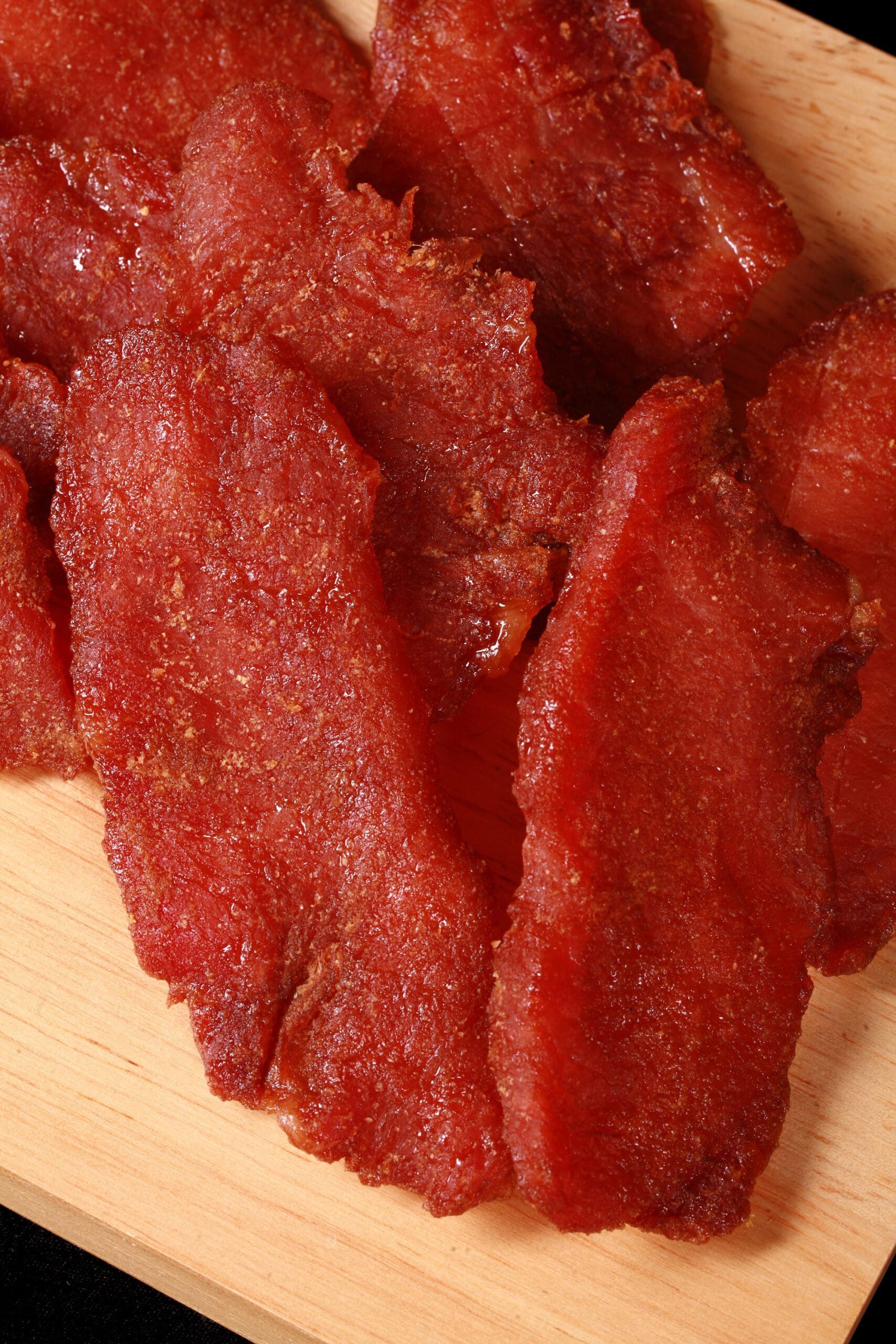 A pile of pork jerky slices on a wooden cutting board.