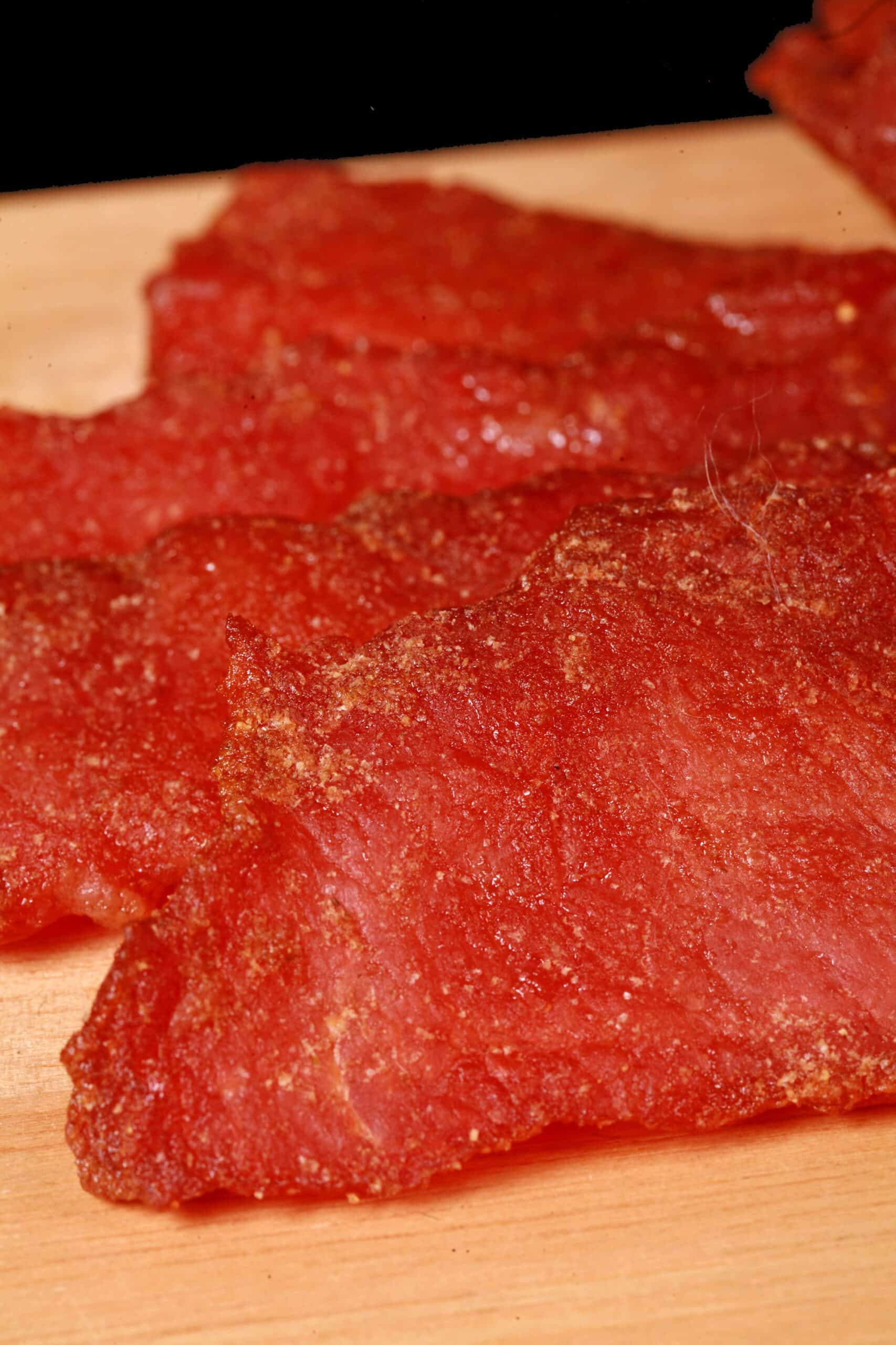A pile of pork loin jerky slices on a wooden cutting board.