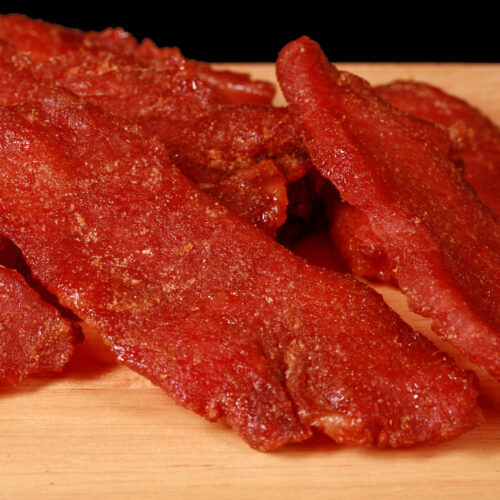 A pile of pork jerky slices on a wooden cutting board.
