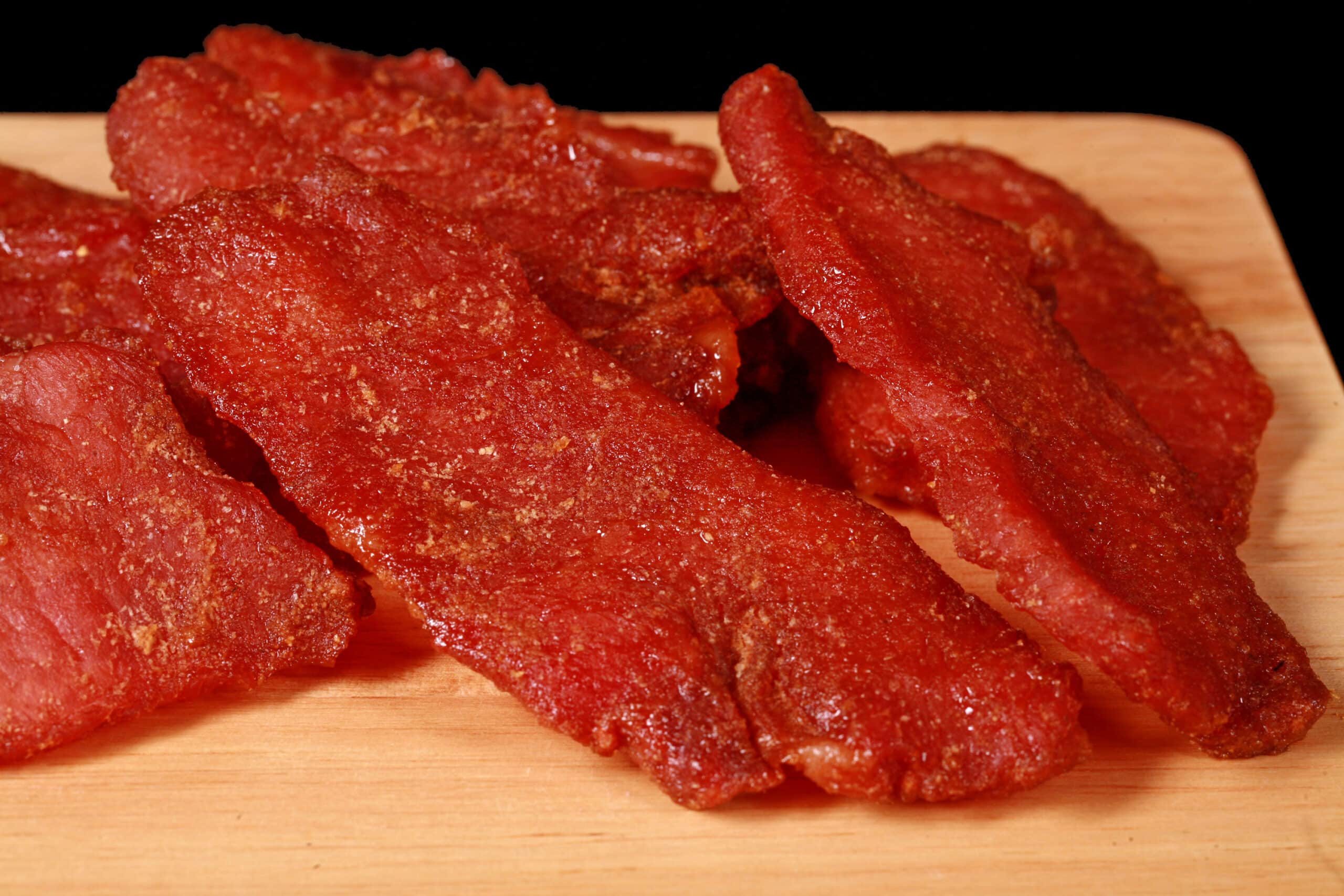 A pile of pork jerky slices on a wooden cutting board.