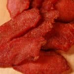 A pile of pork loin jerky slices on a wooden cutting board.