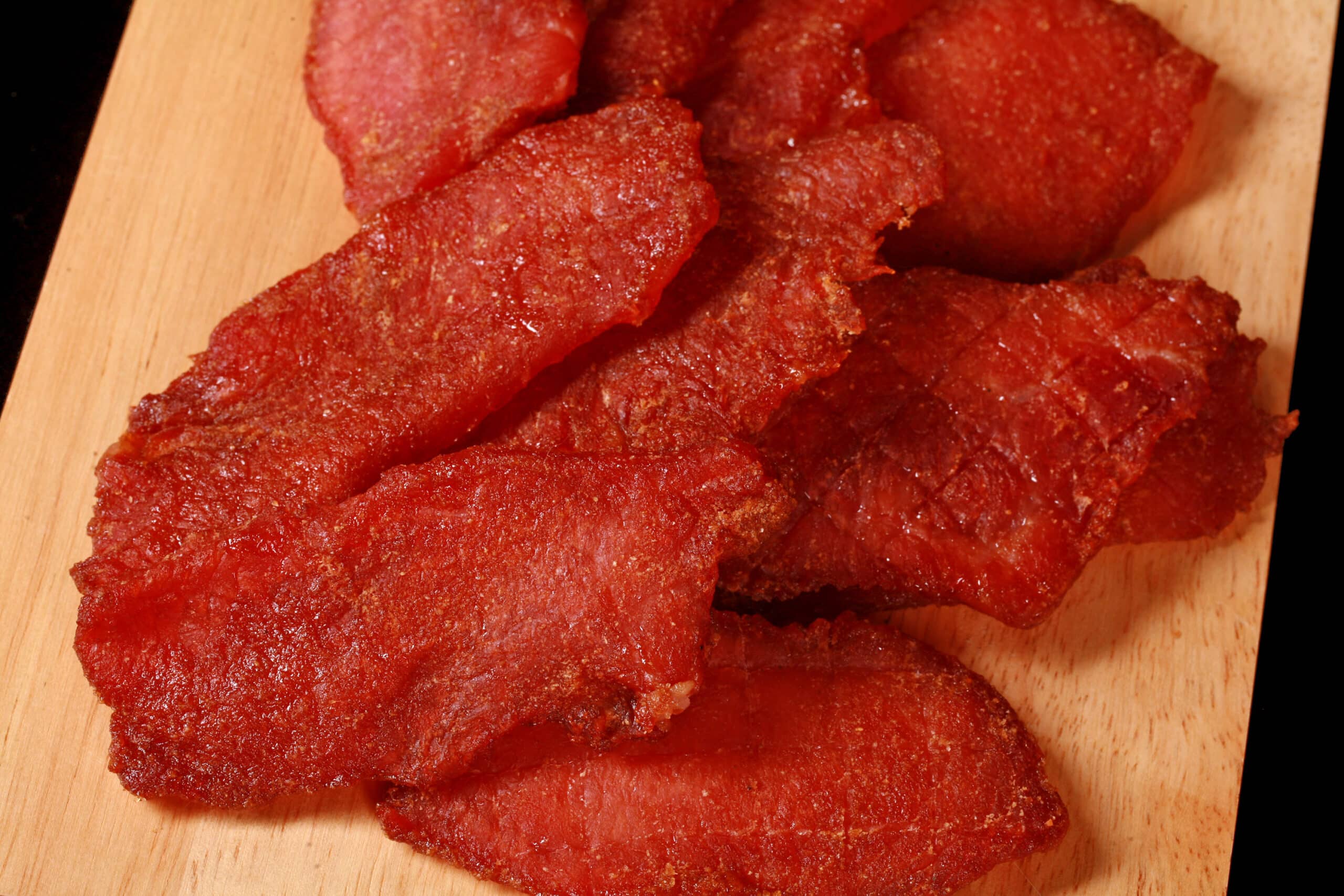A pile of pork loin jerky slices on a wooden cutting board.