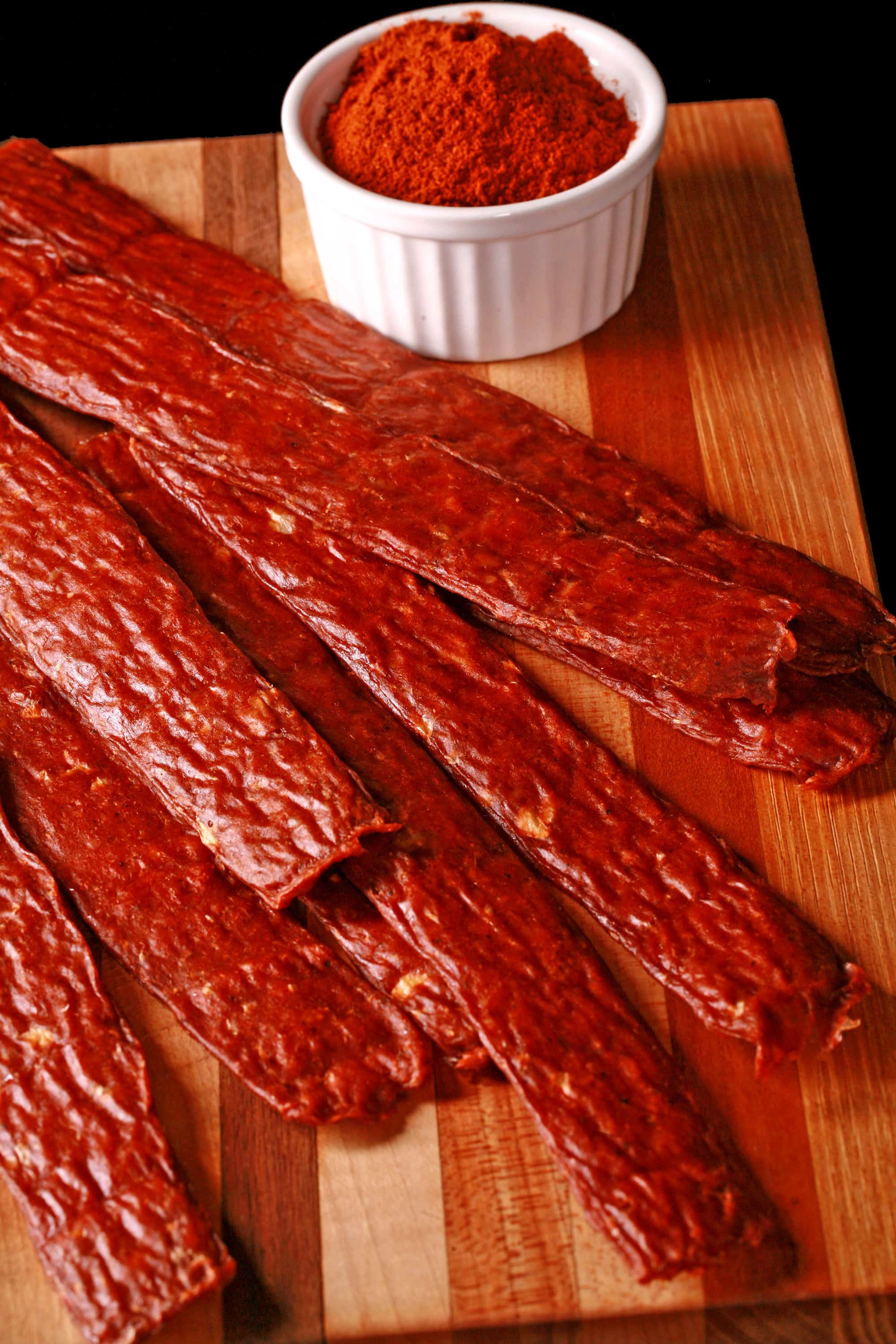 Several strips of berbere ground chicken jerky on a cutting board with a ramekin of berbere seasoning.