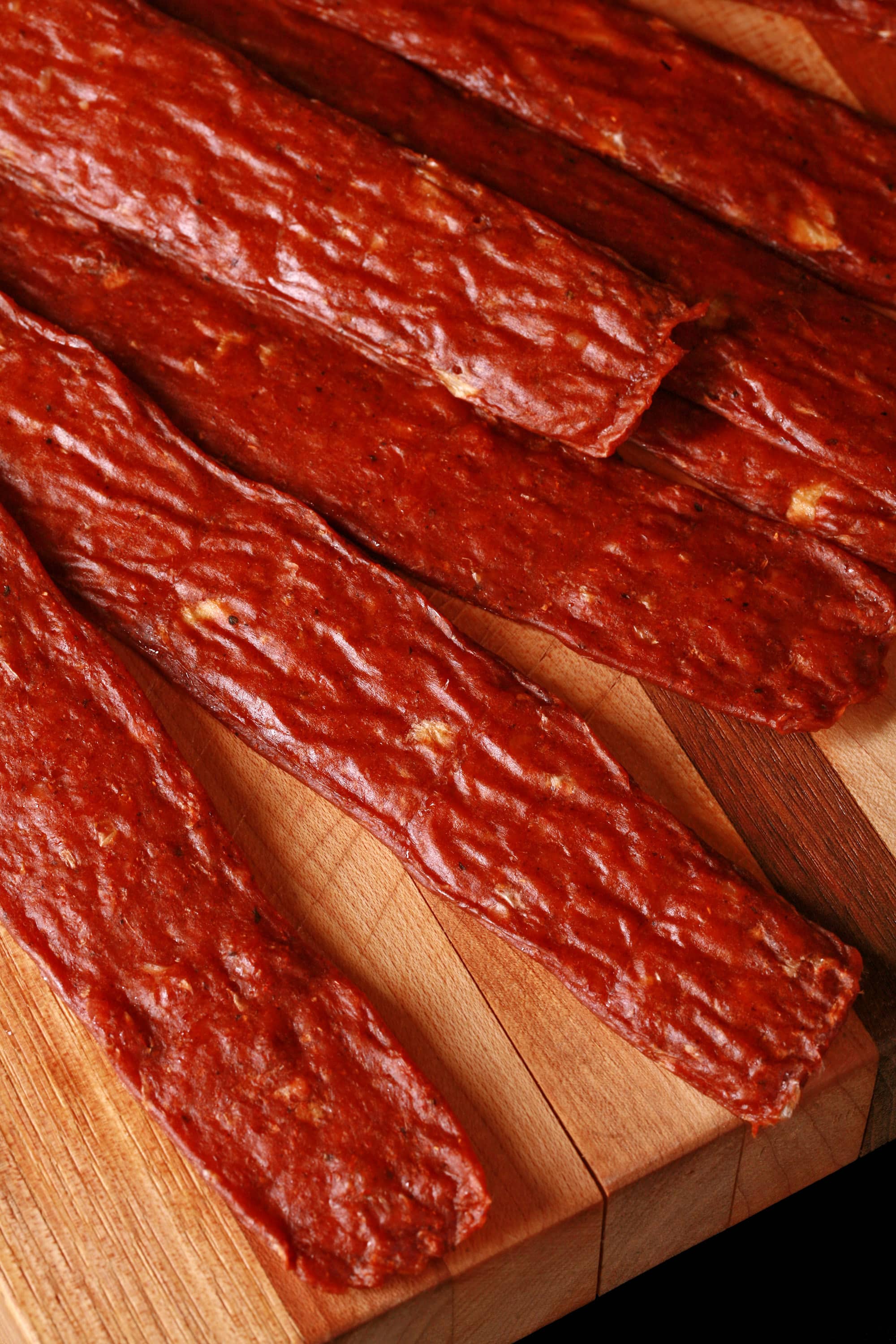 Several strips of berbere chicken jerky on a cutting board with a ramekin of berbere seasoning.