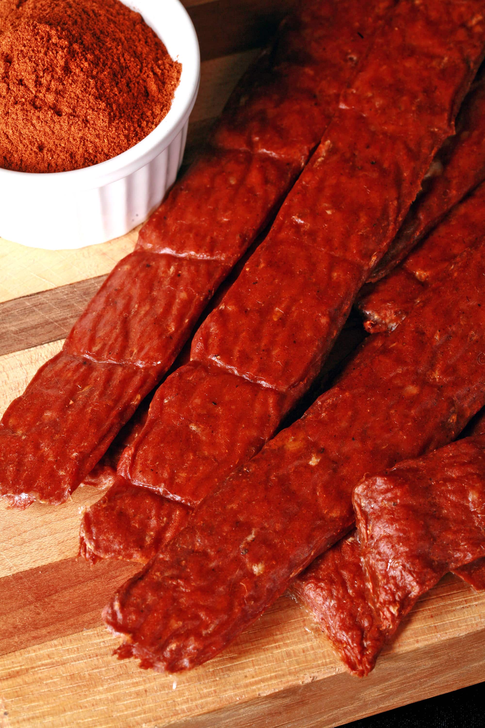 Several strips of berbere ground chicken jerky on a cutting board with a ramekin of berbere seasoning.