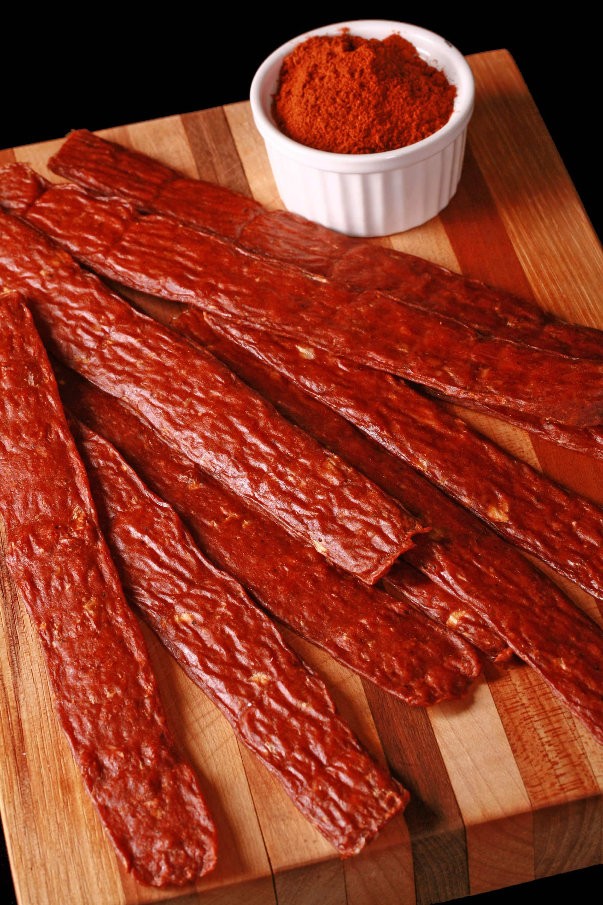 Several strips of berbere chicken jerky on a cutting board with a ramekin of berbere seasoning.