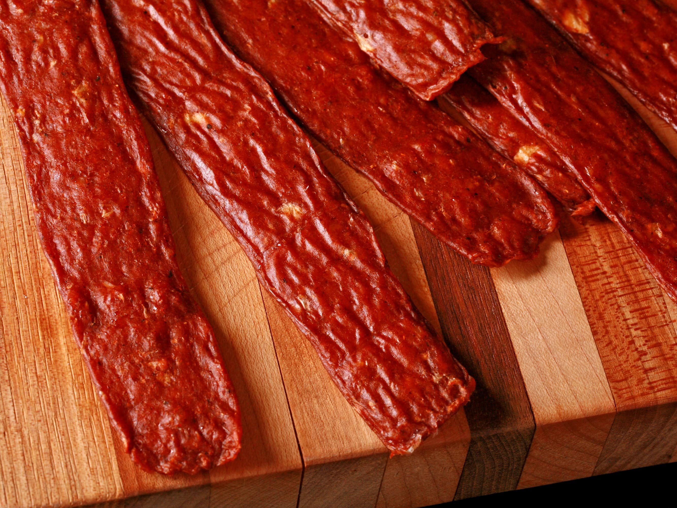 Several strips of berbere ground chicken jerky on a cutting board with a ramekin of berbere seasoning.
