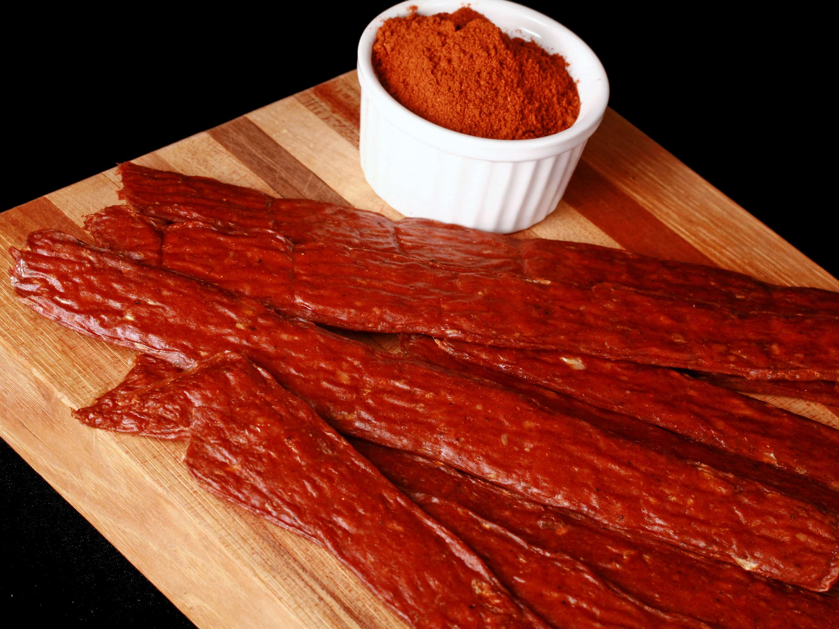Several strips of berbere chicken jerky on a cutting board with a ramekin of berbere seasoning.