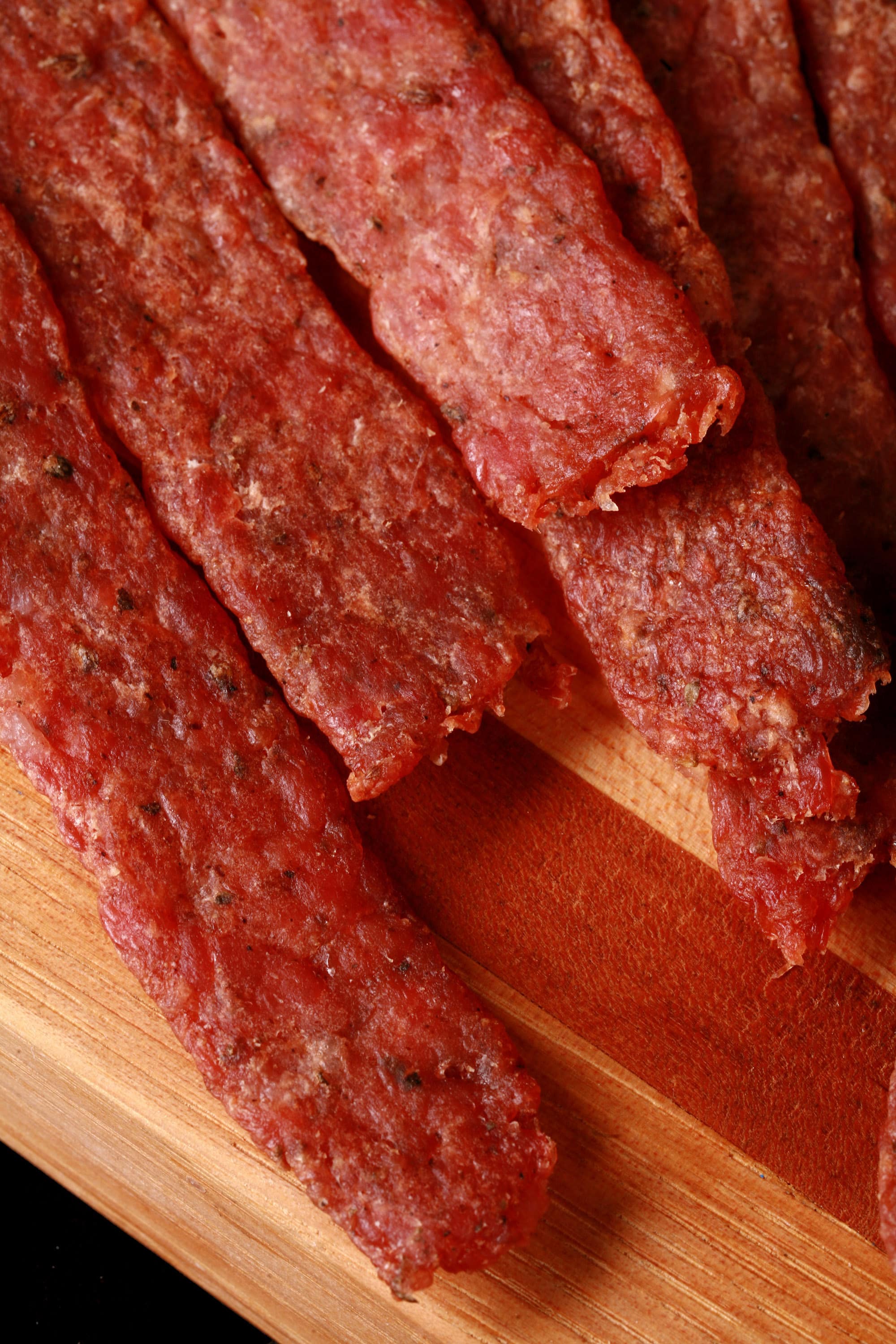 Several strips of bratwurst jerky on a cutting board.