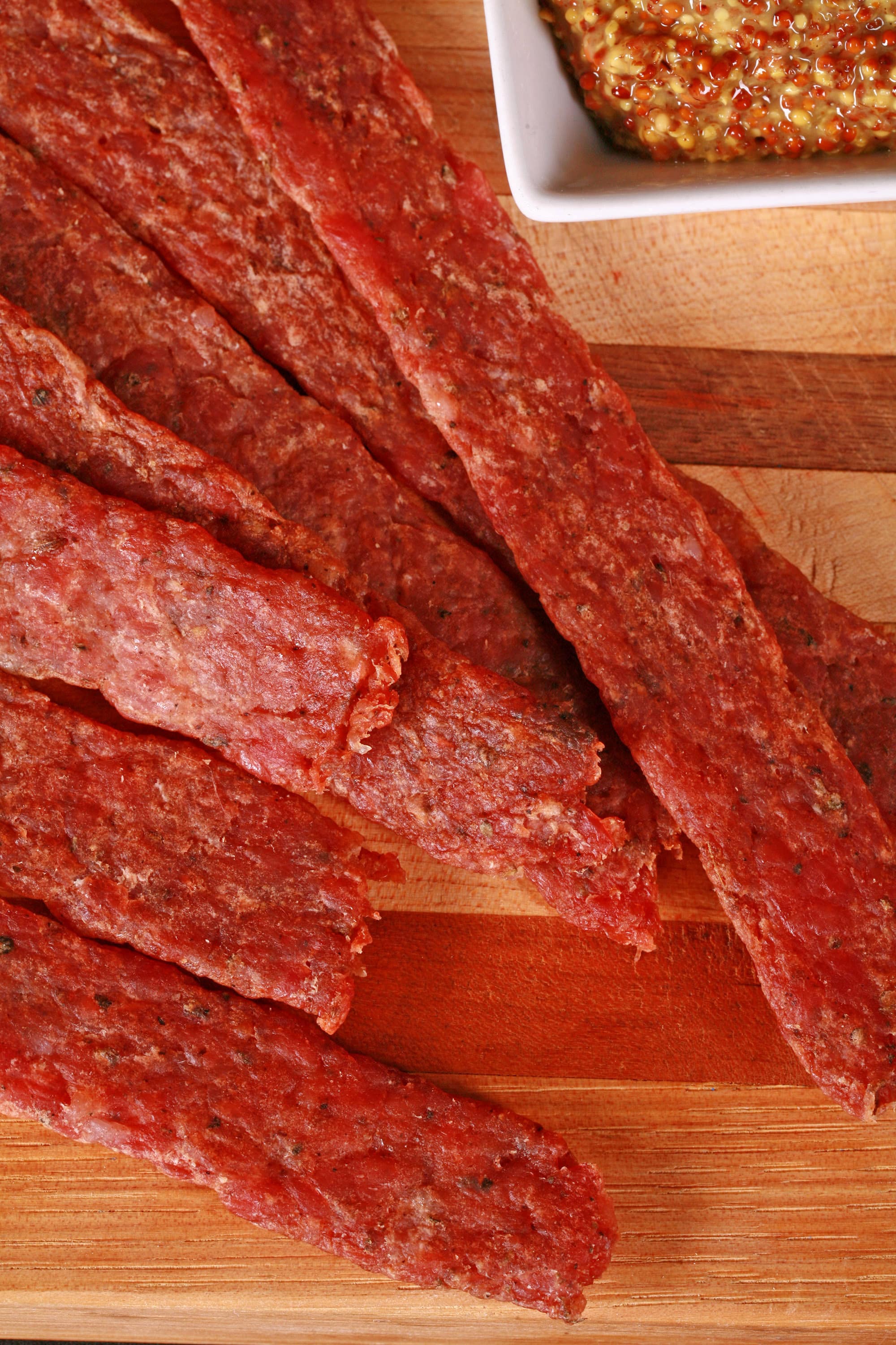 Several strips of bratwurst flavoured ground pork jerky on a cutting board.
