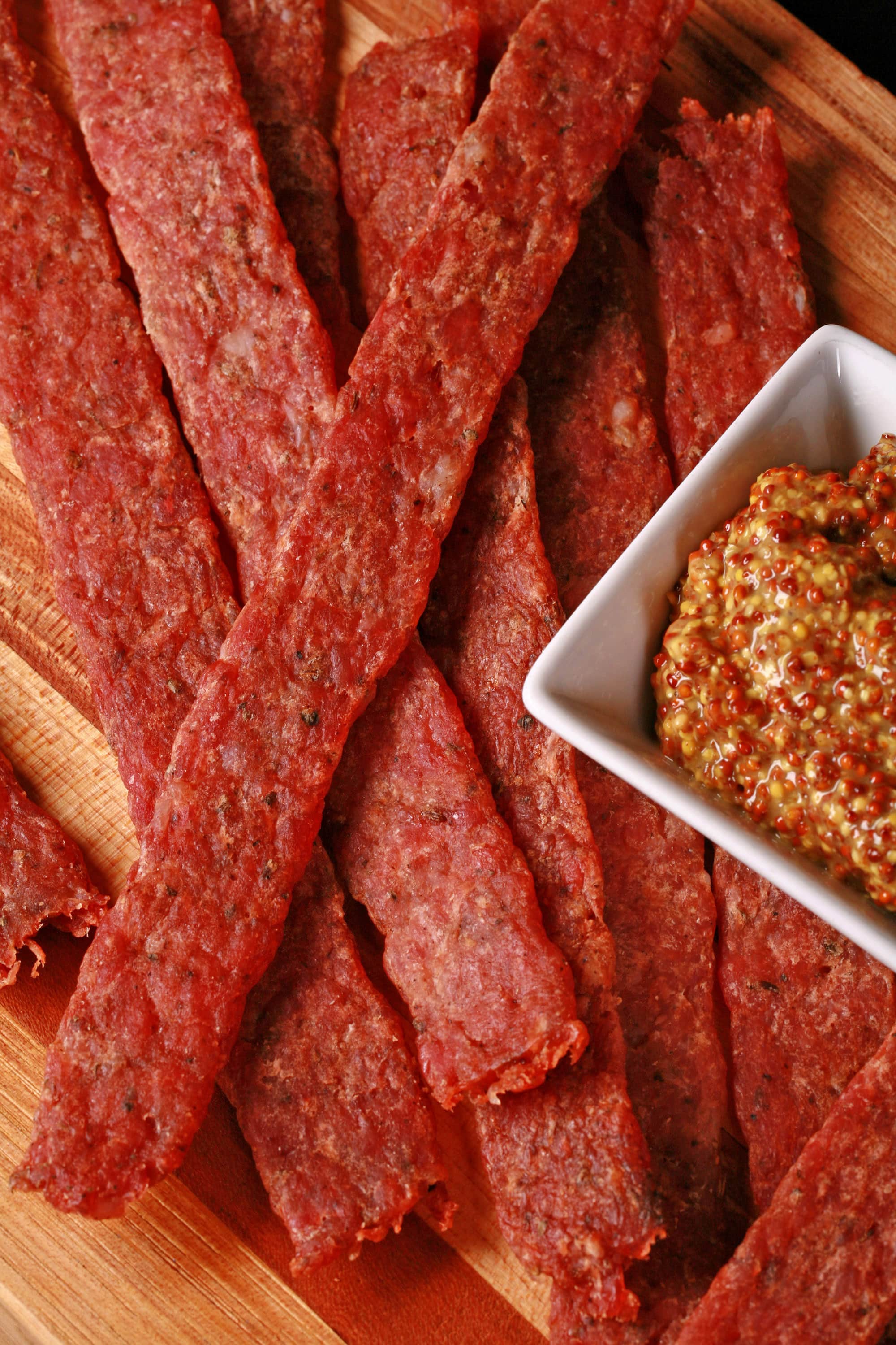 Several strips of bratwurst flavoured ground pork jerky on a cutting board.