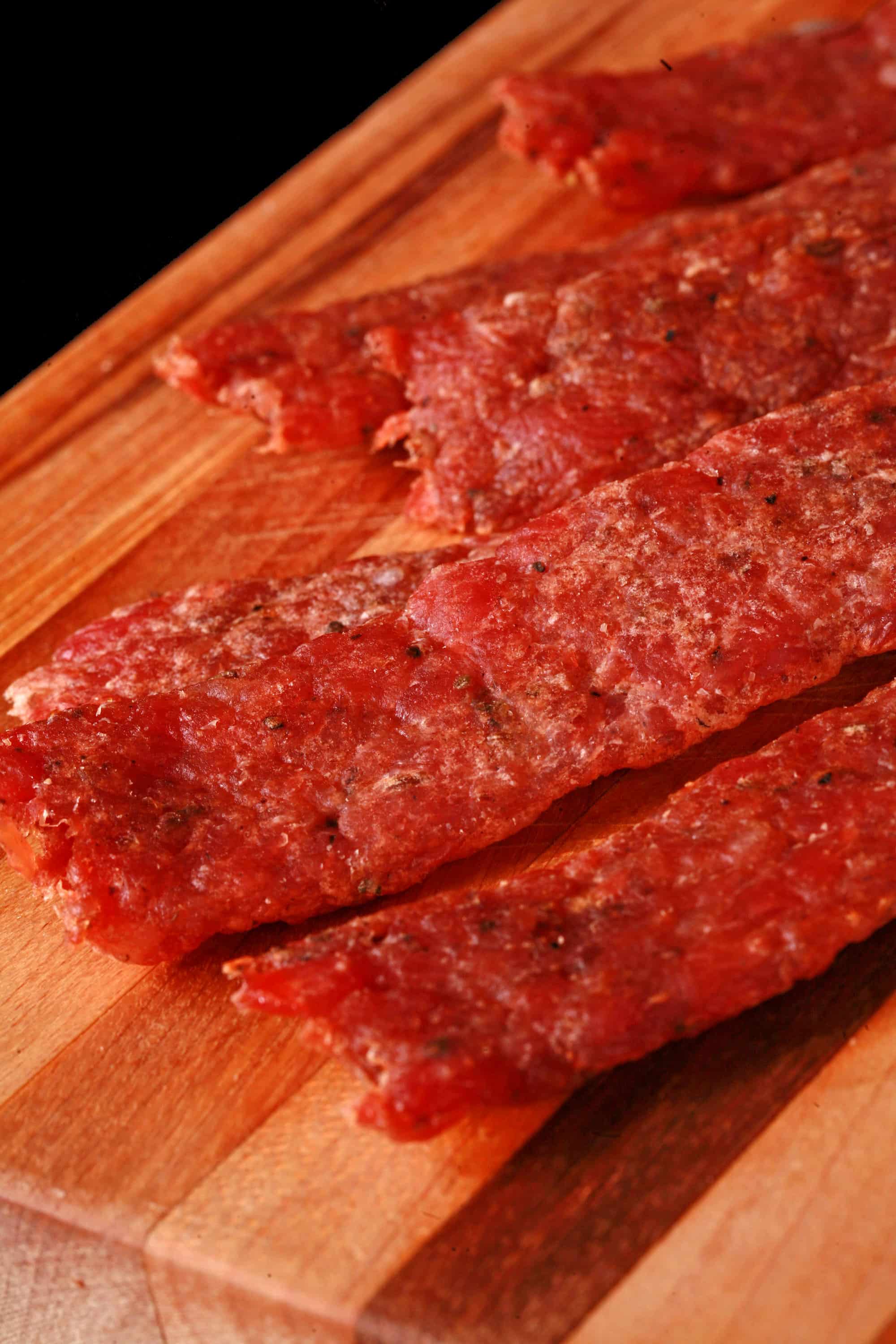 Several strips of bratwurst jerky on a cutting board.