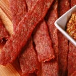Several strips of bratwurst flavoured ground pork jerky on a cutting board.