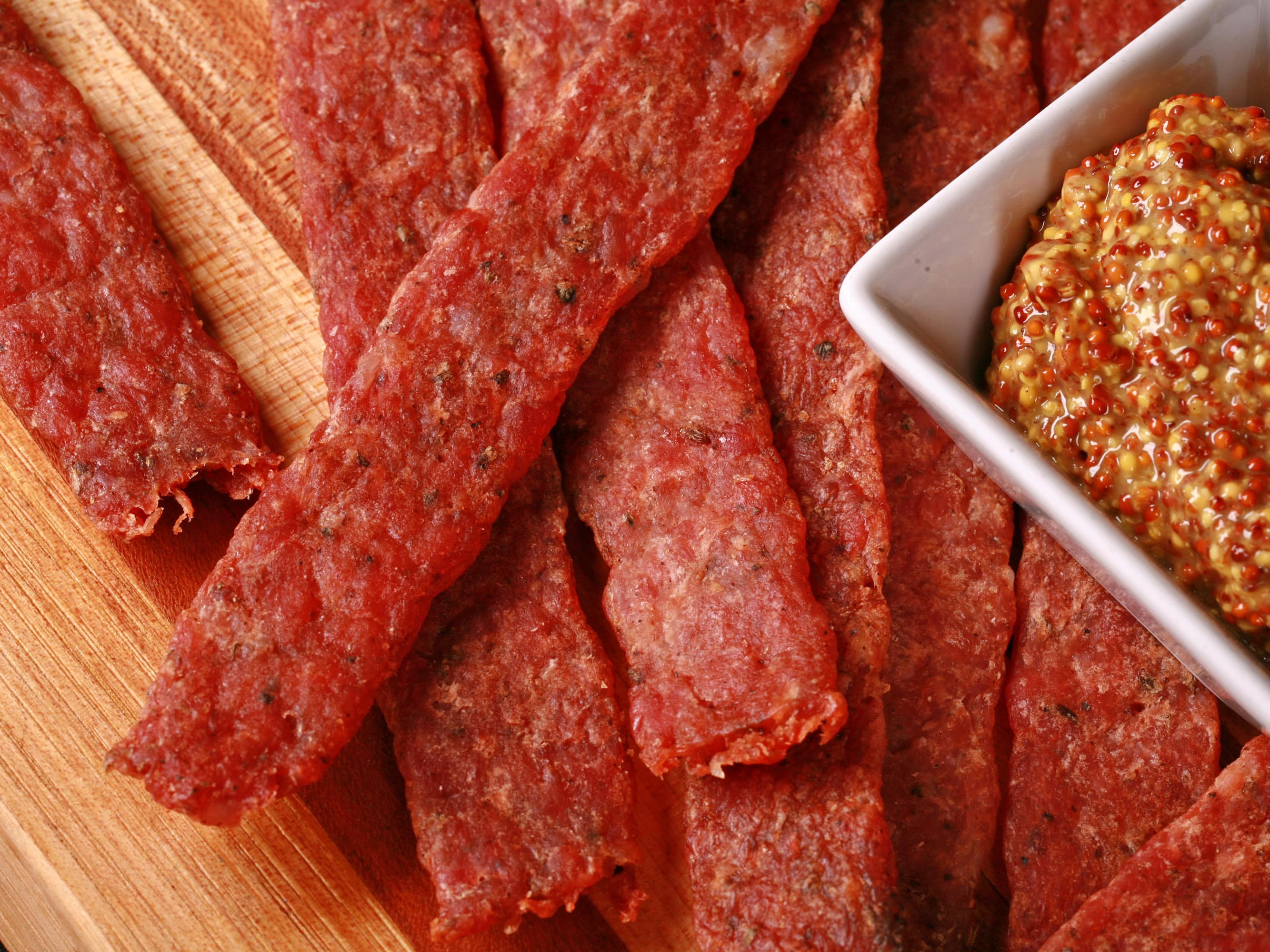 Several strips of bratwurst flavoured ground pork jerky on a cutting board.