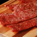Several strips of bratwurst jerky on a cutting board.