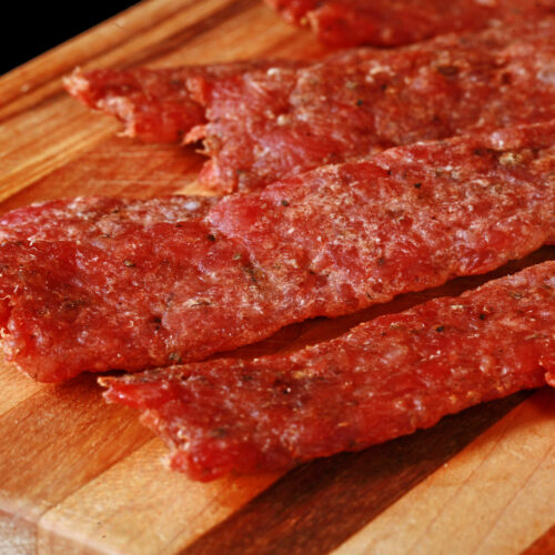 Several strips of bratwurst jerky on a cutting board.