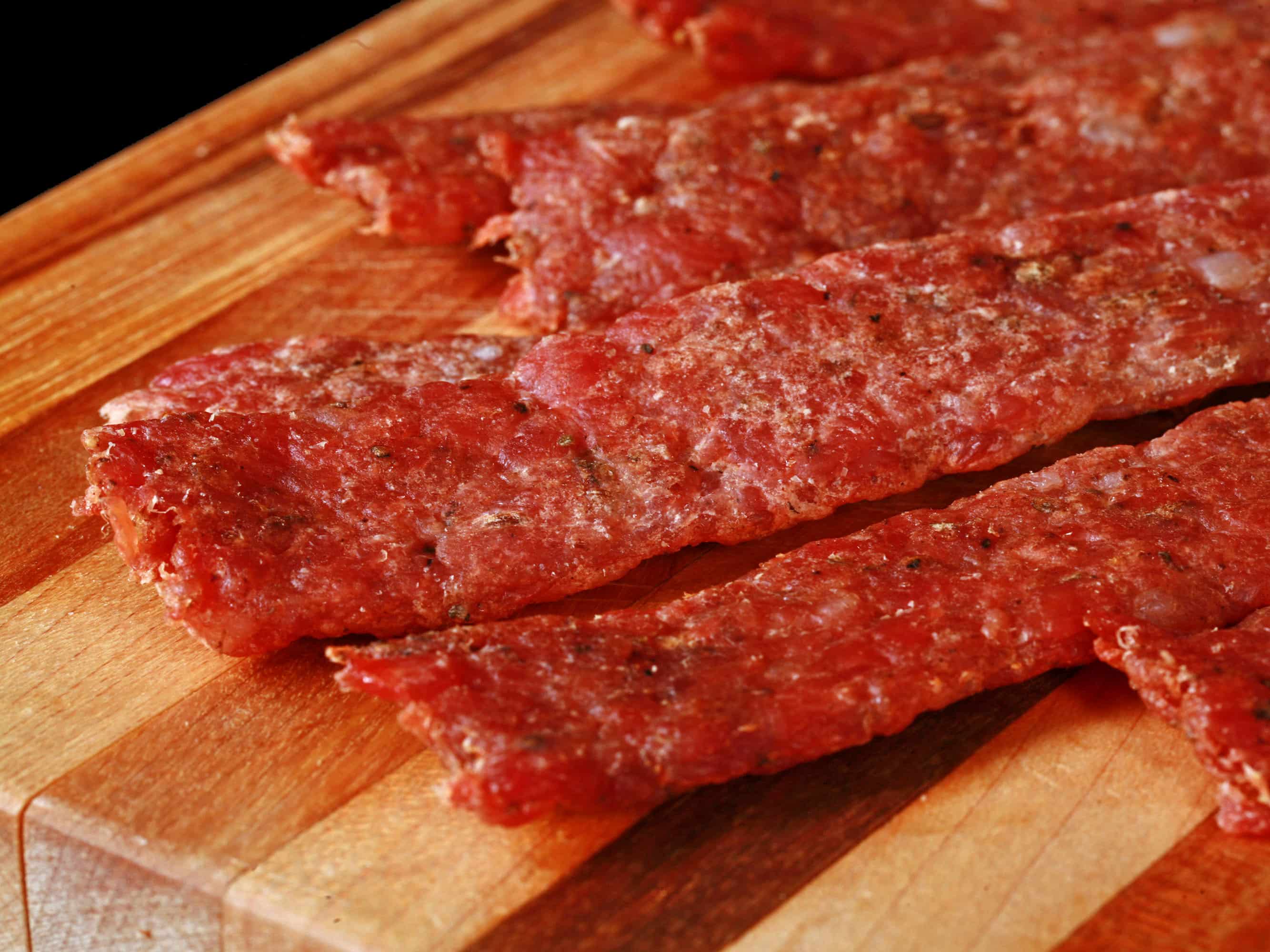 Several strips of bratwurst jerky on a cutting board.