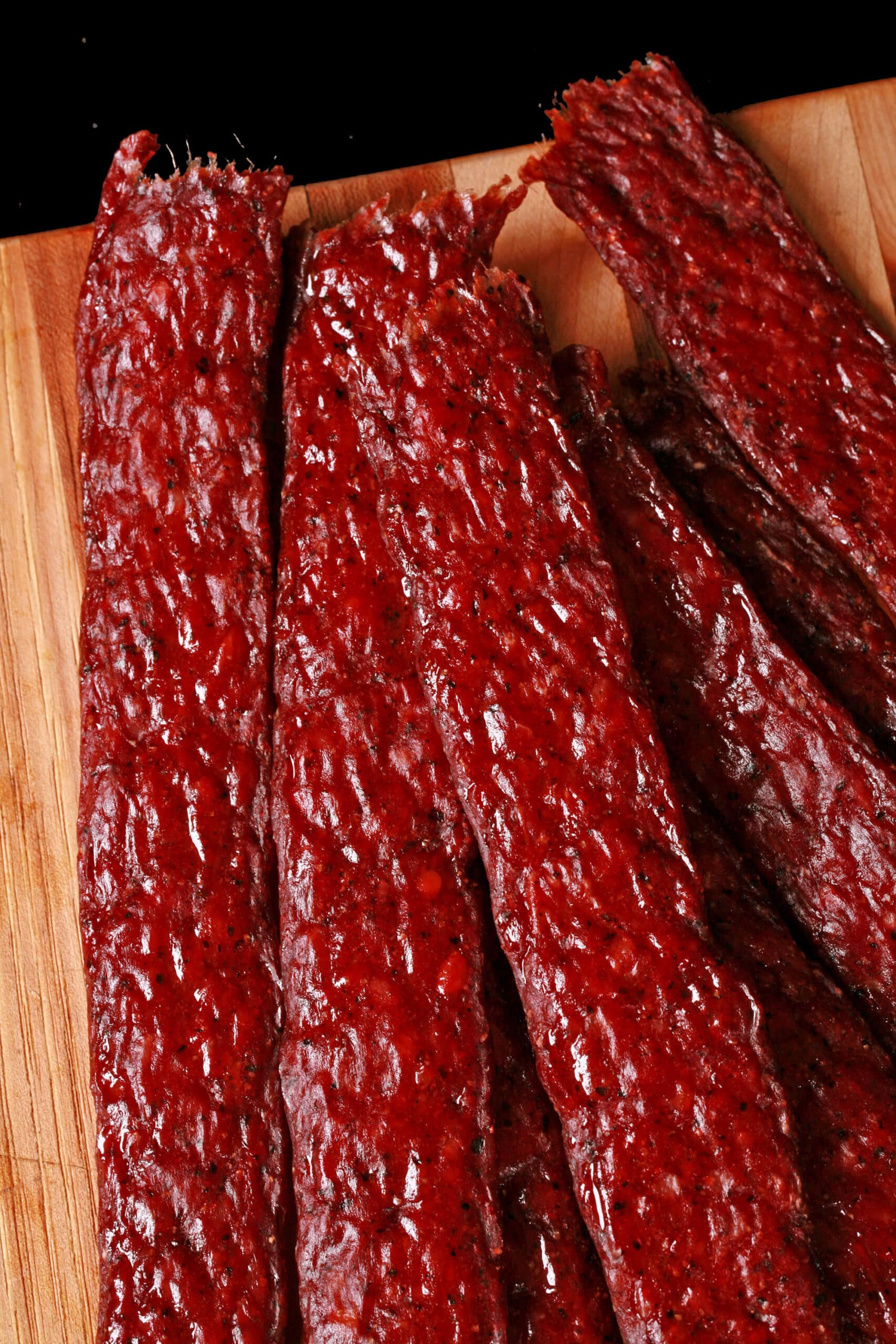 Several strips of homemade peppered beef jerky on a wooden cutting board.