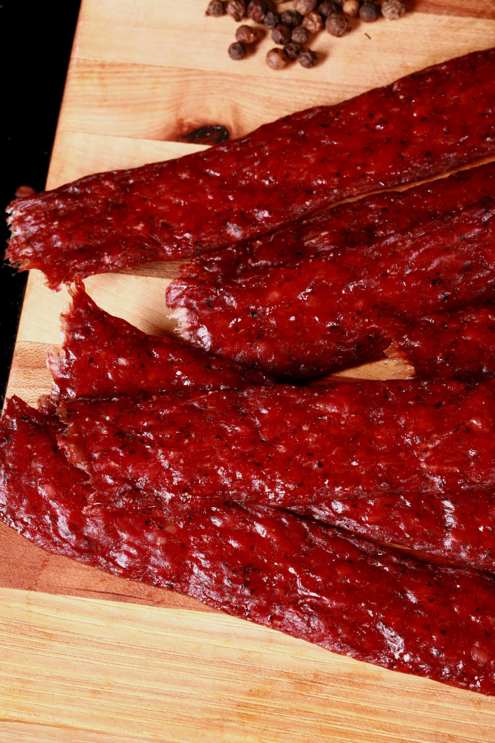 Several strips of homemade peppered ground beef jerky on a wooden cutting board.