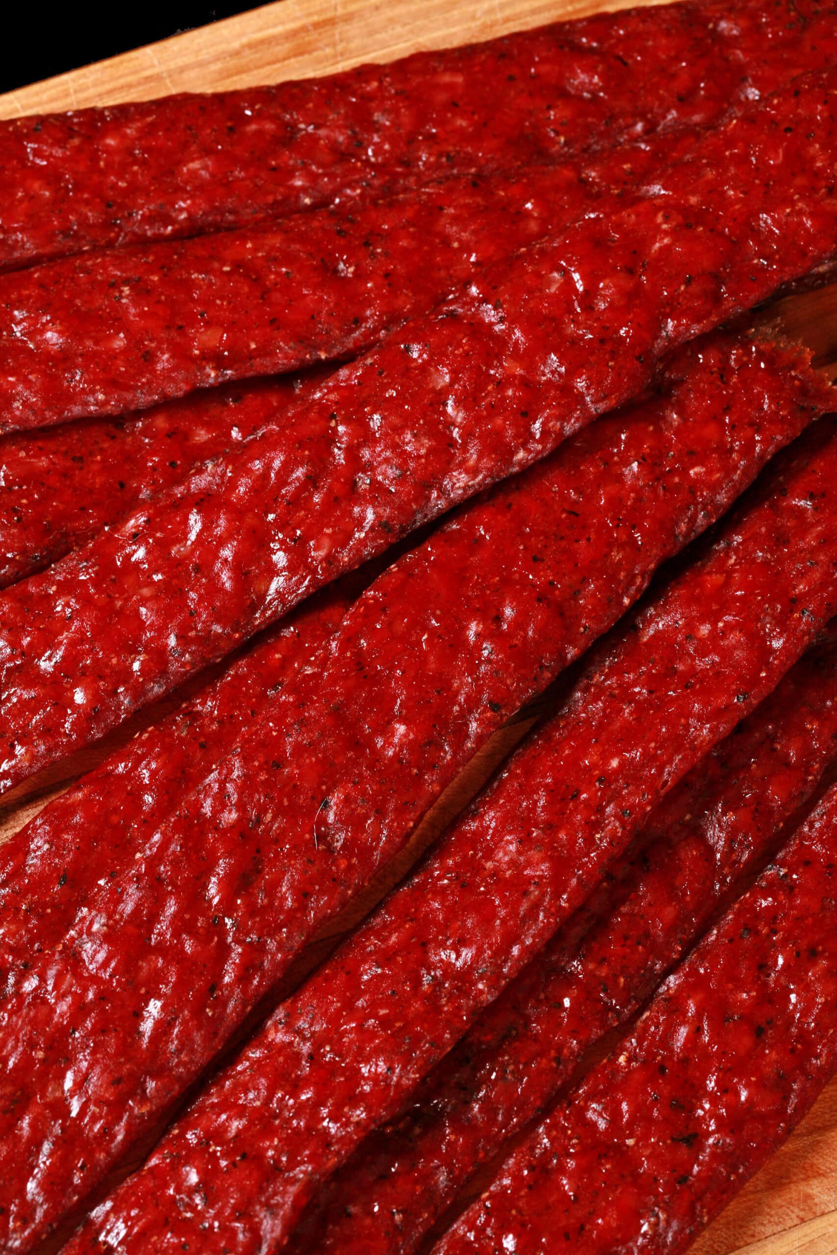 Several strips of homemade peppered beef jerky on a wooden cutting board.