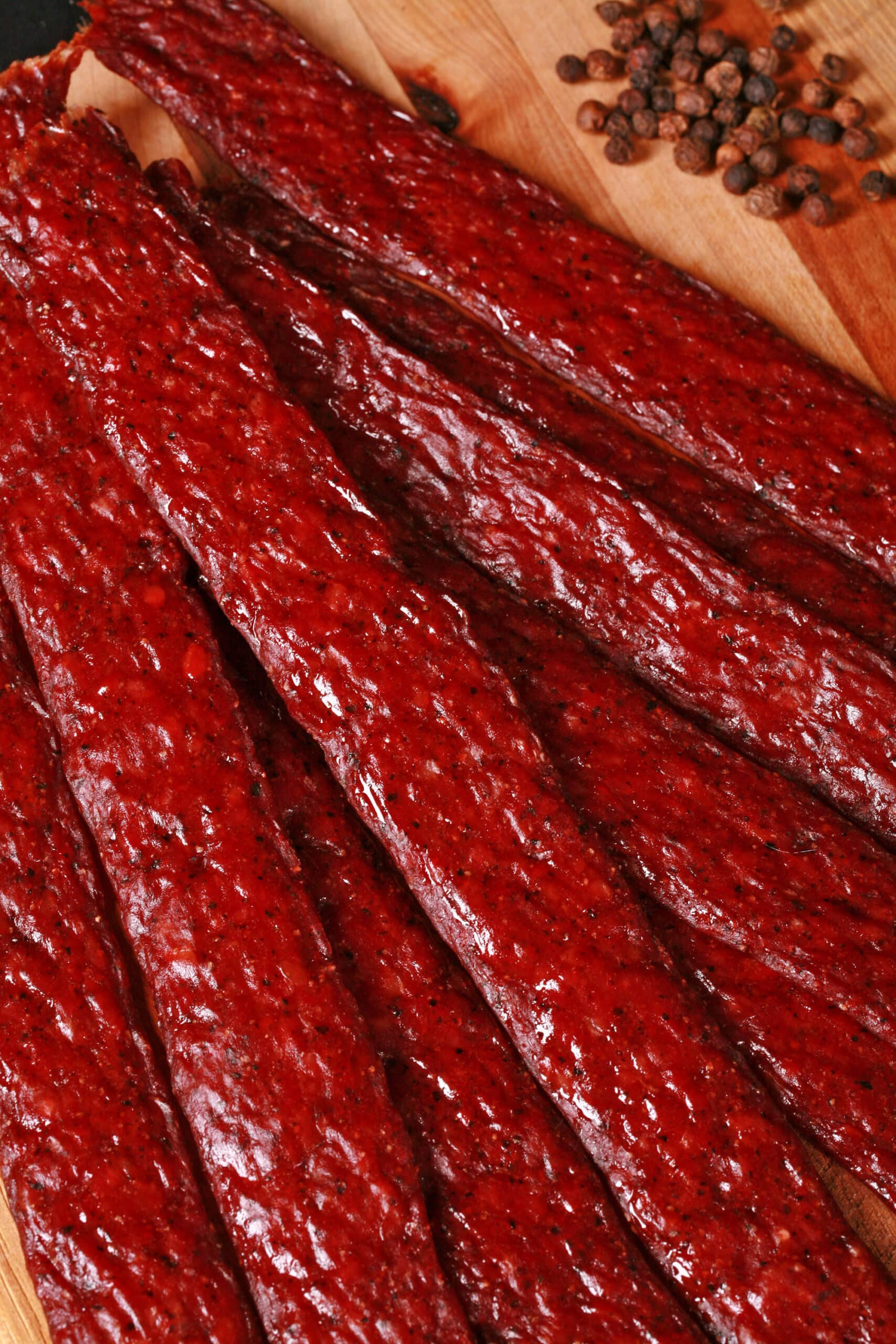 Several strips of homemade peppered ground beef jerky on a wooden cutting board.