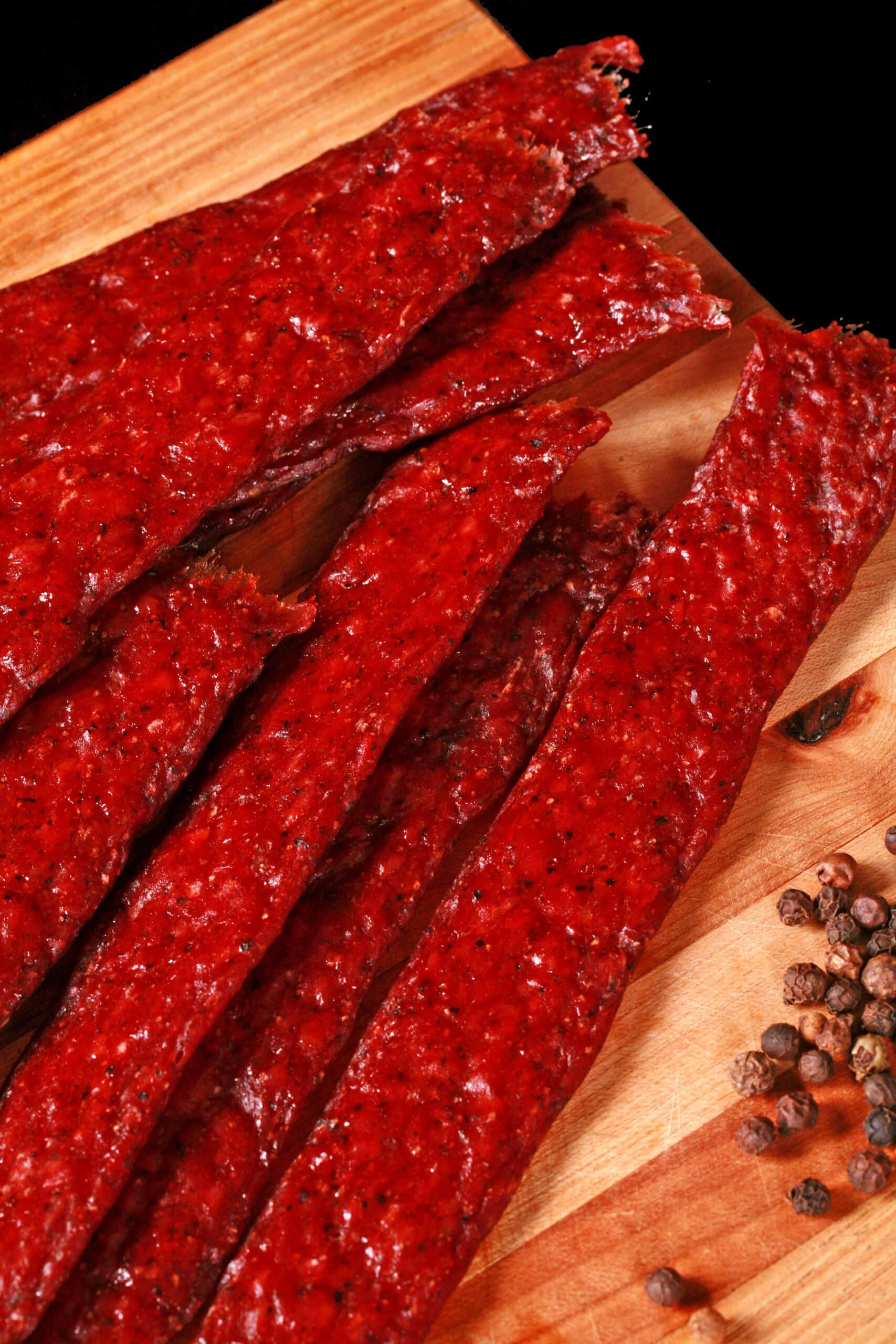 Several strips of homemade peppered beef jerky on a wooden cutting board.