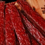 Several strips of homemade peppered ground beef jerky on a wooden cutting board.