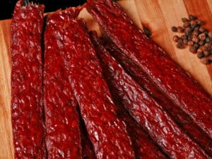 Several strips of homemade peppered ground beef jerky on a wooden cutting board.