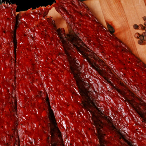 Several strips of homemade peppered ground beef jerky on a wooden cutting board.