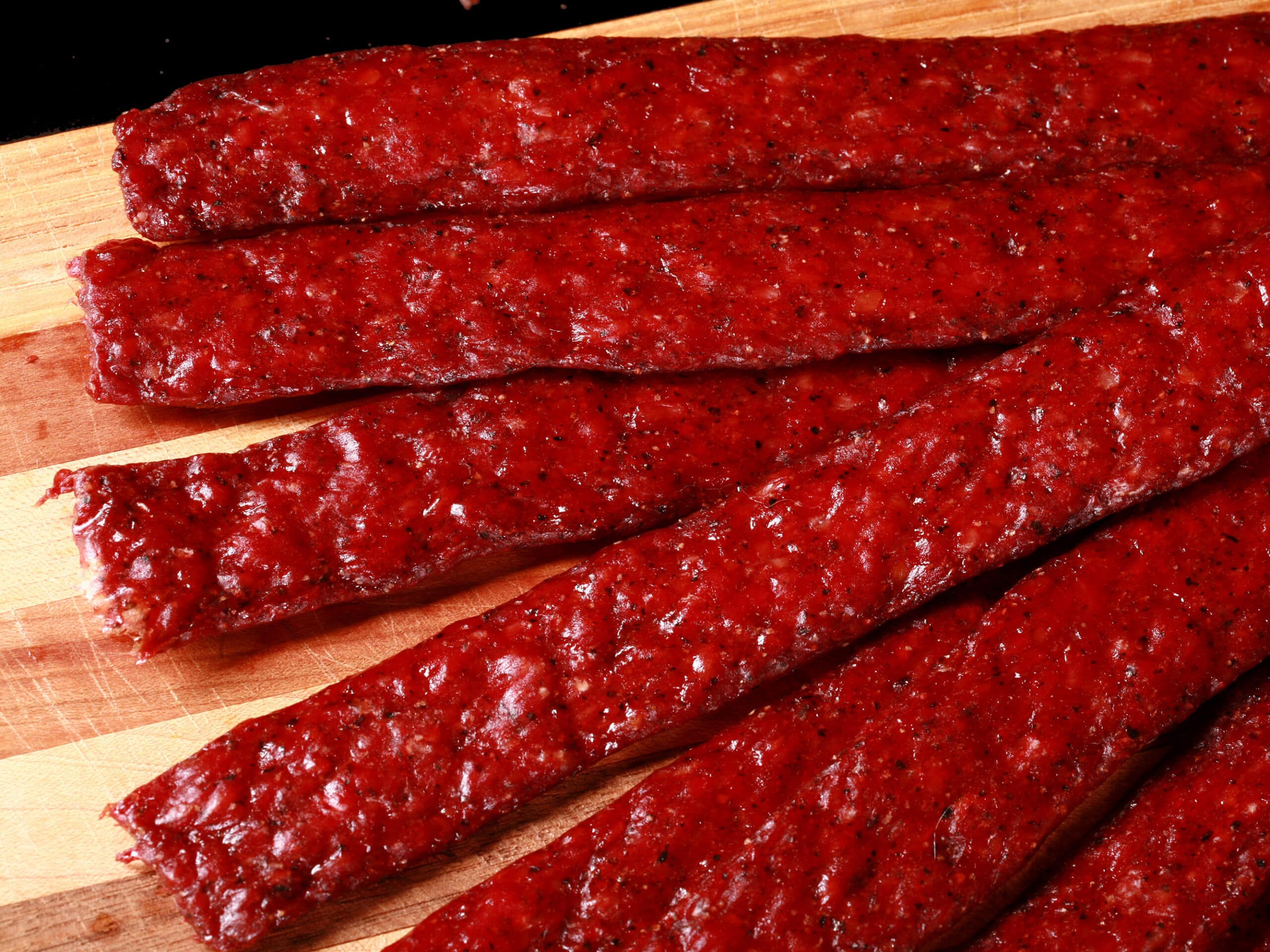 Several strips of homemade peppered beef jerky on a wooden cutting board.