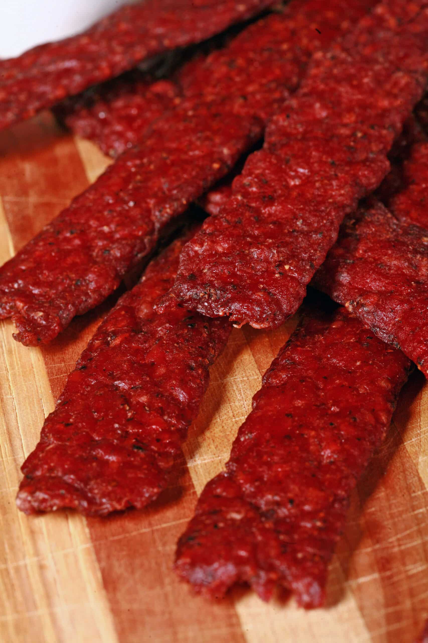 Peppered ground venison jerky strips on a wooden cutting board.