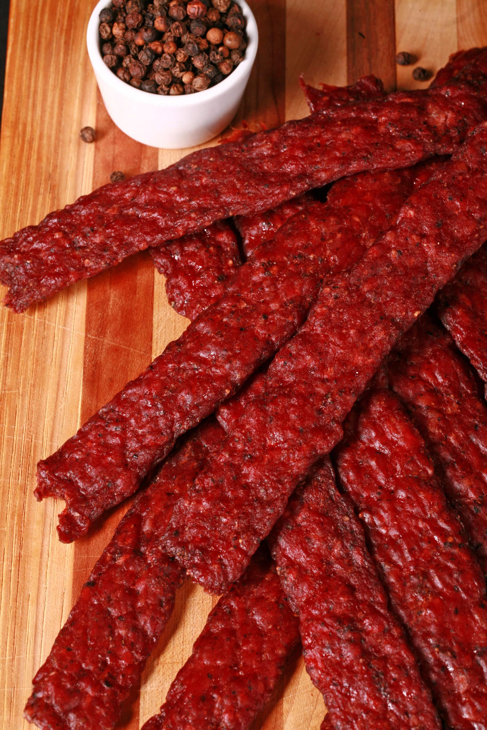 Peppered ground venison jerky strips on a wooden cutting board.