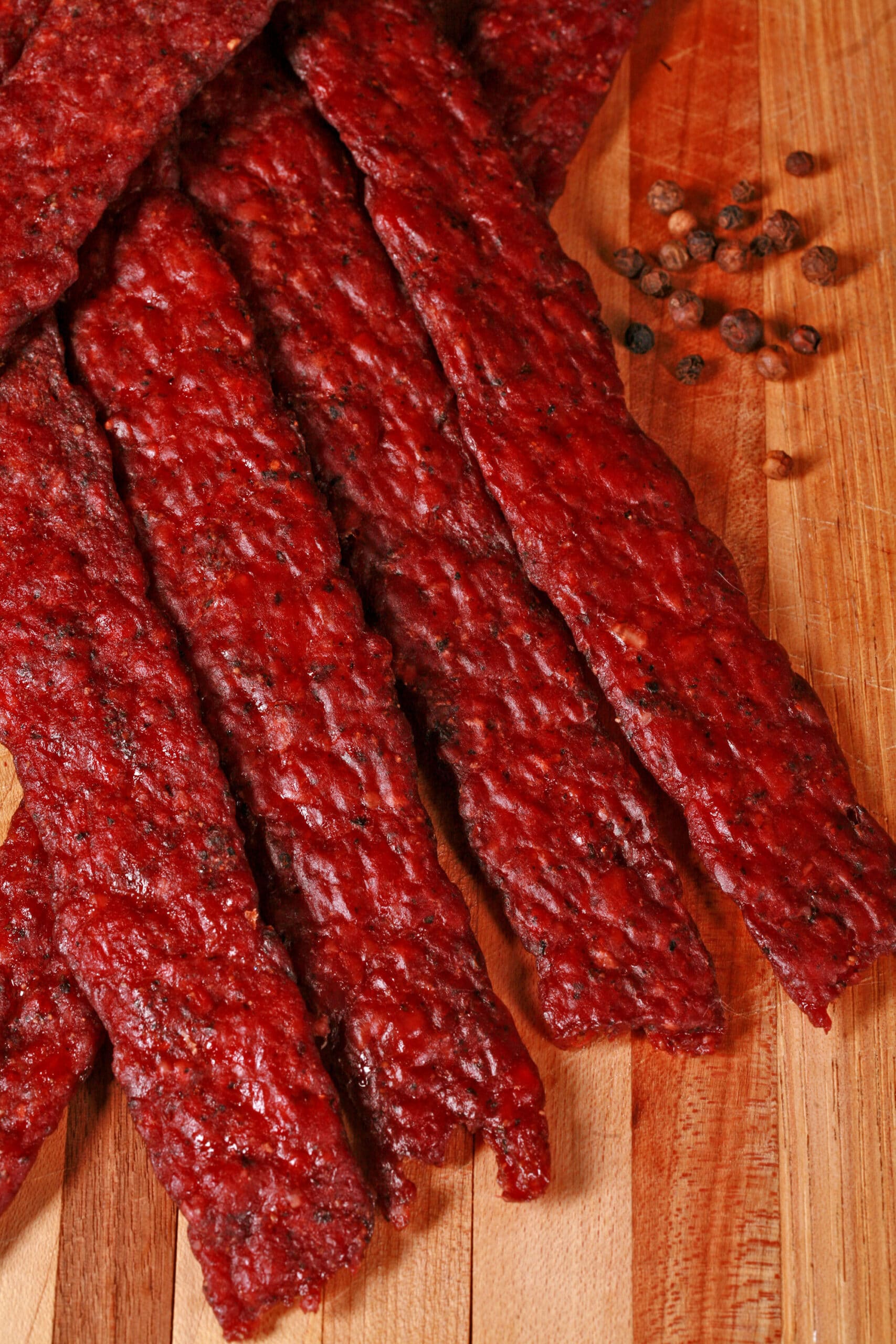Peppered ground deer jerky strips on a wooden cutting board.
