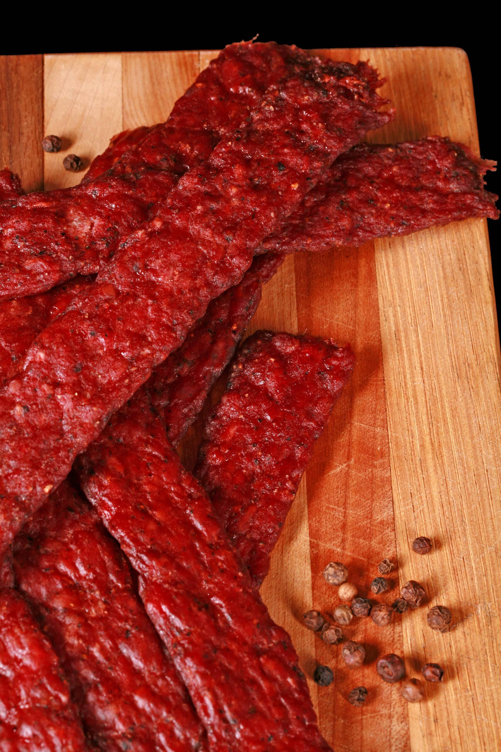 Peppered ground venison jerky strips on a wooden cutting board.