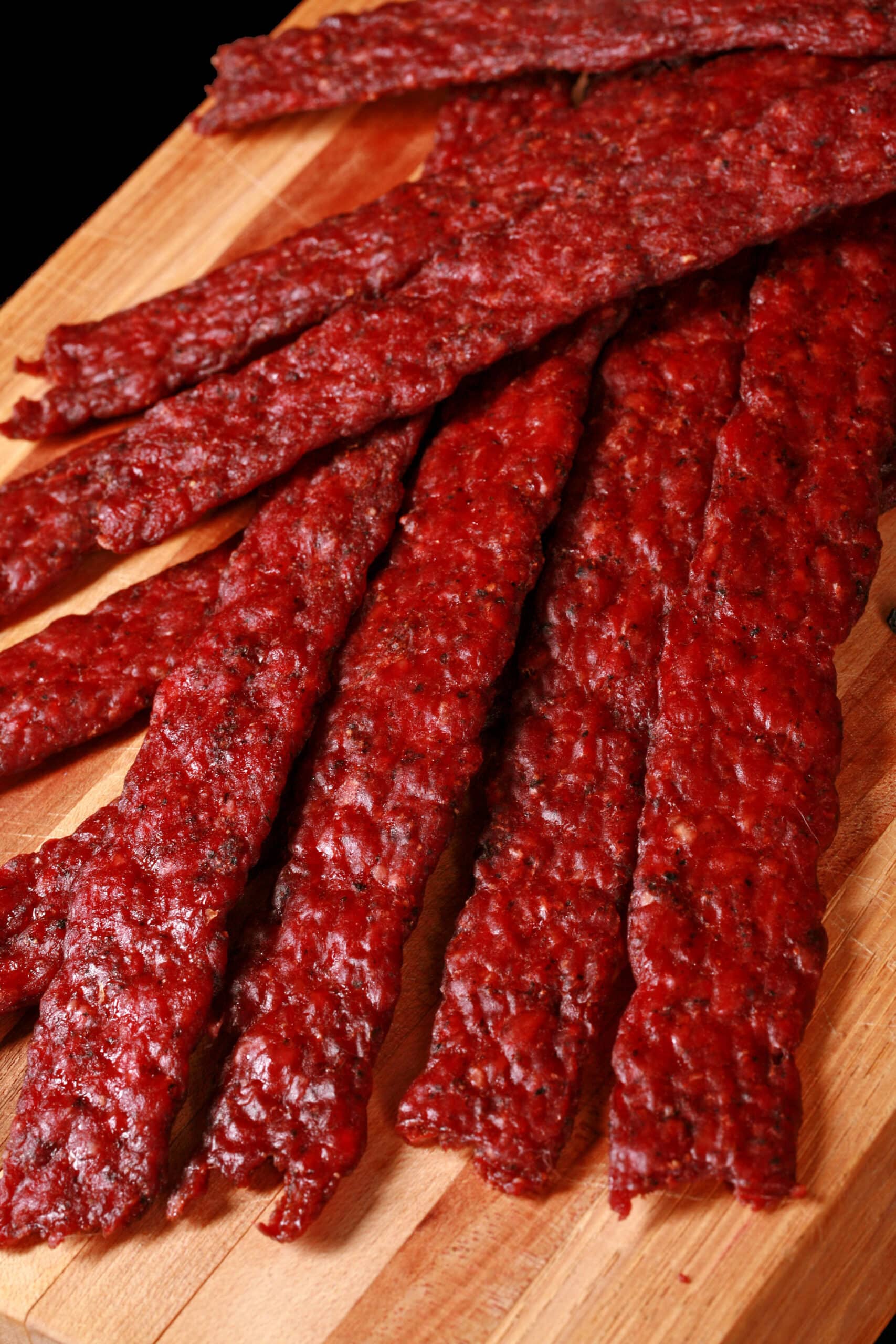 Peppered ground deer jerky strips on a wooden cutting board.
