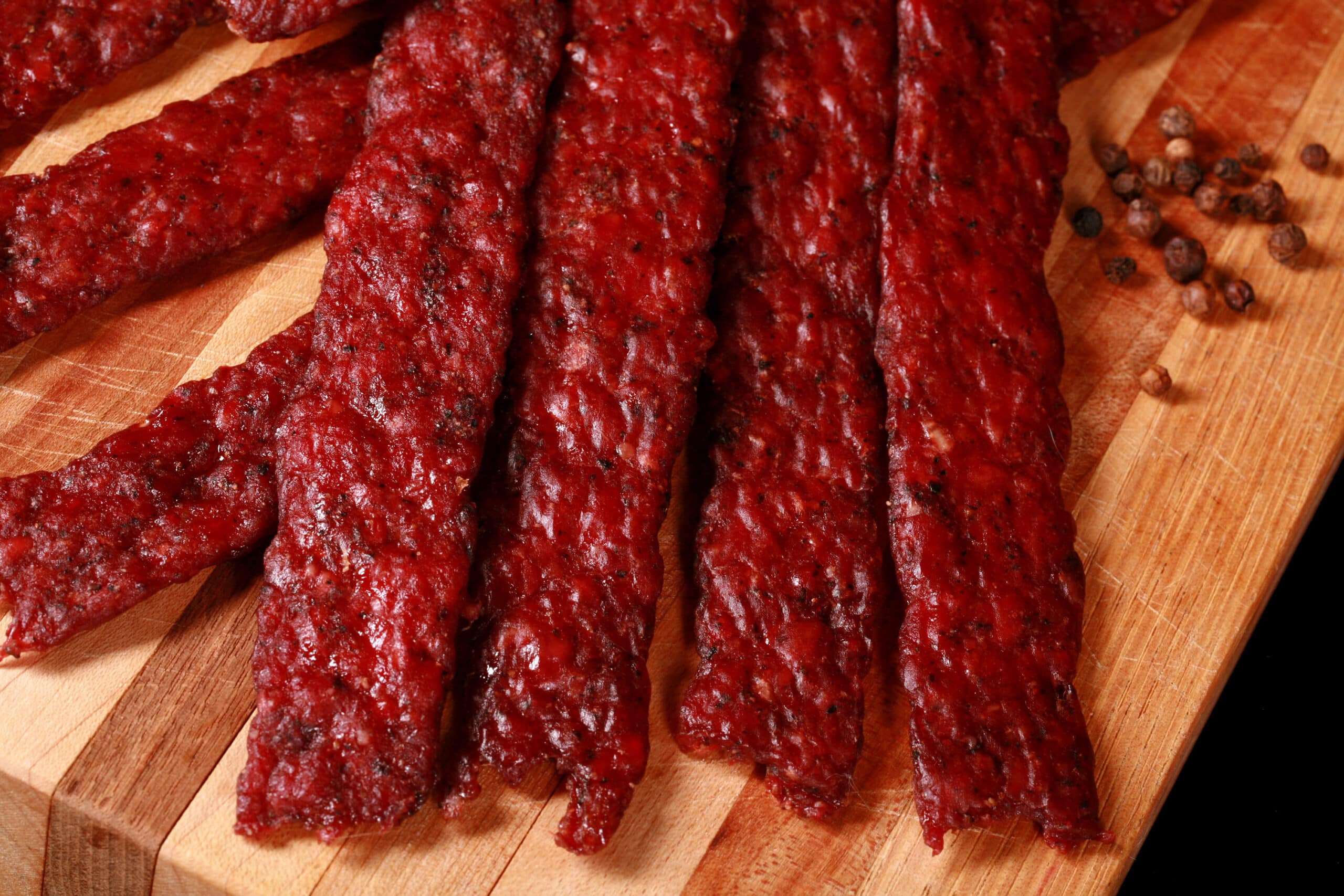 Peppered ground venison jerky strips on a wooden cutting board.