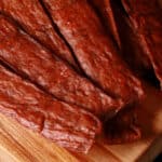 Several strips of swedish potato sausage ground chicken jerky on a cutting board.