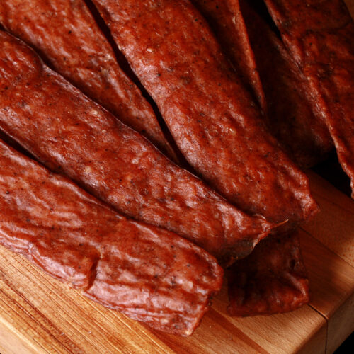 Several strips of swedish potato sausage ground chicken jerky on a cutting board.