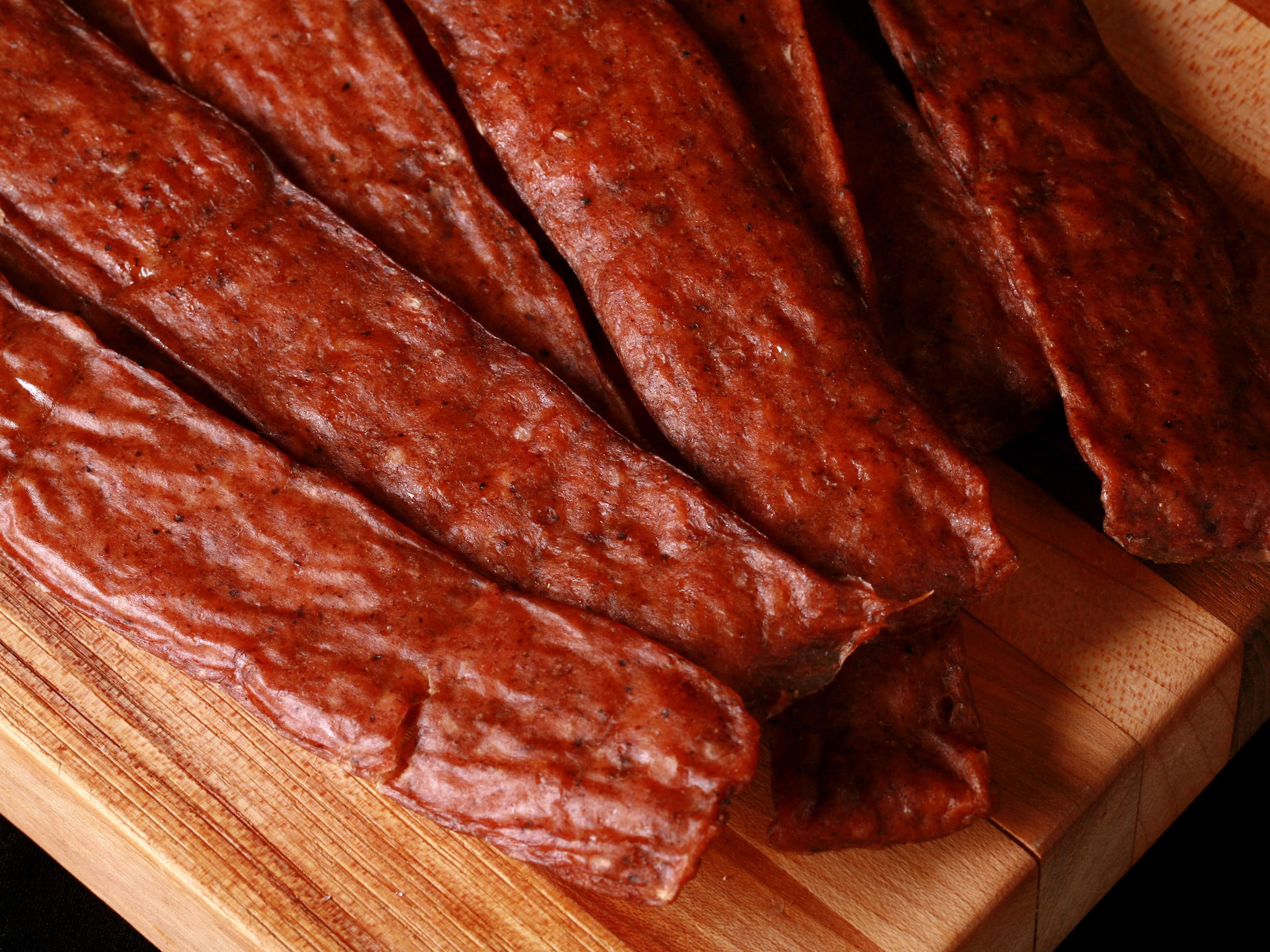 Several strips of swedish potato sausage ground chicken jerky on a cutting board.