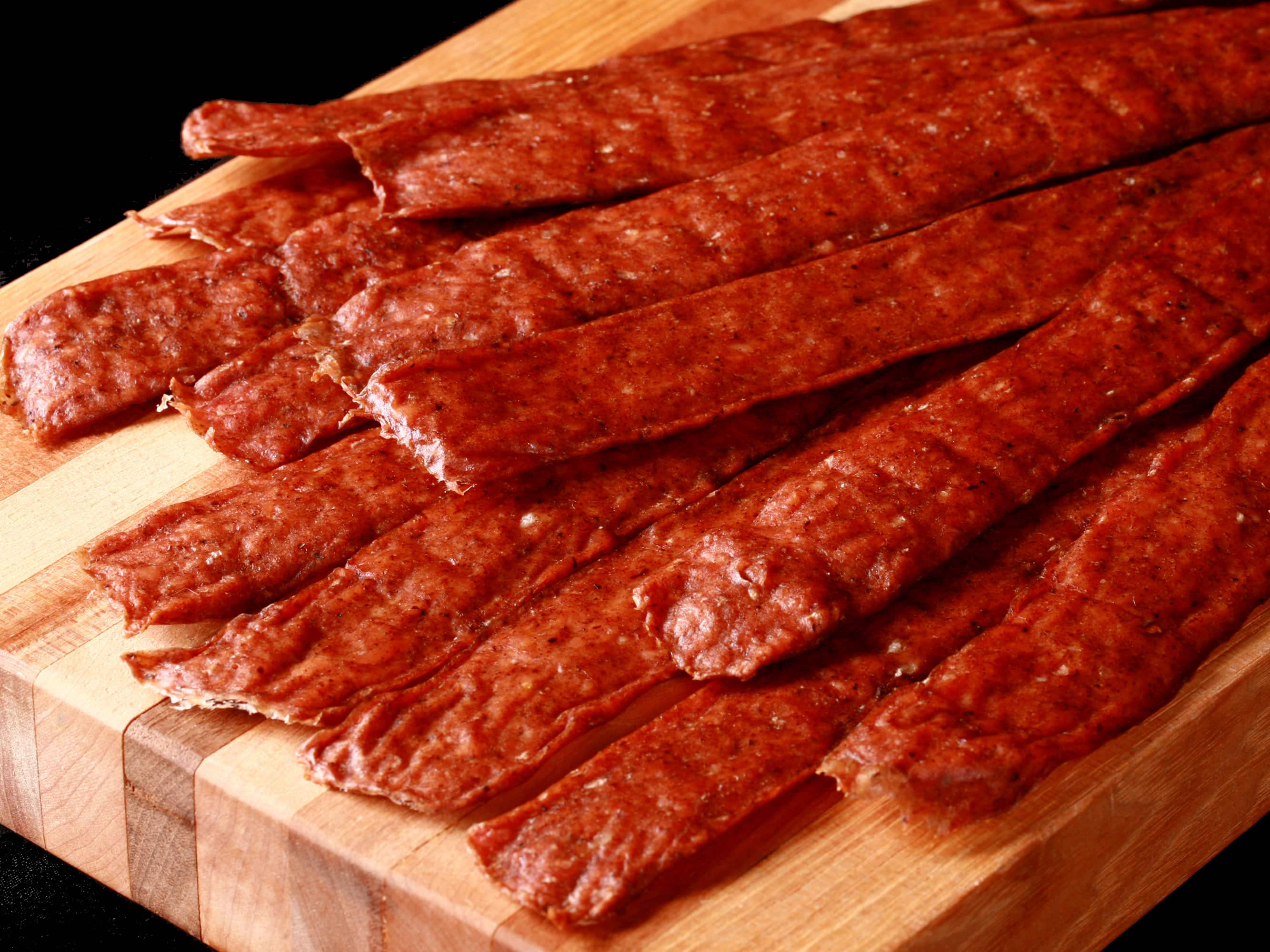 Several strips of swedish potato sausage jerky on a cutting board.