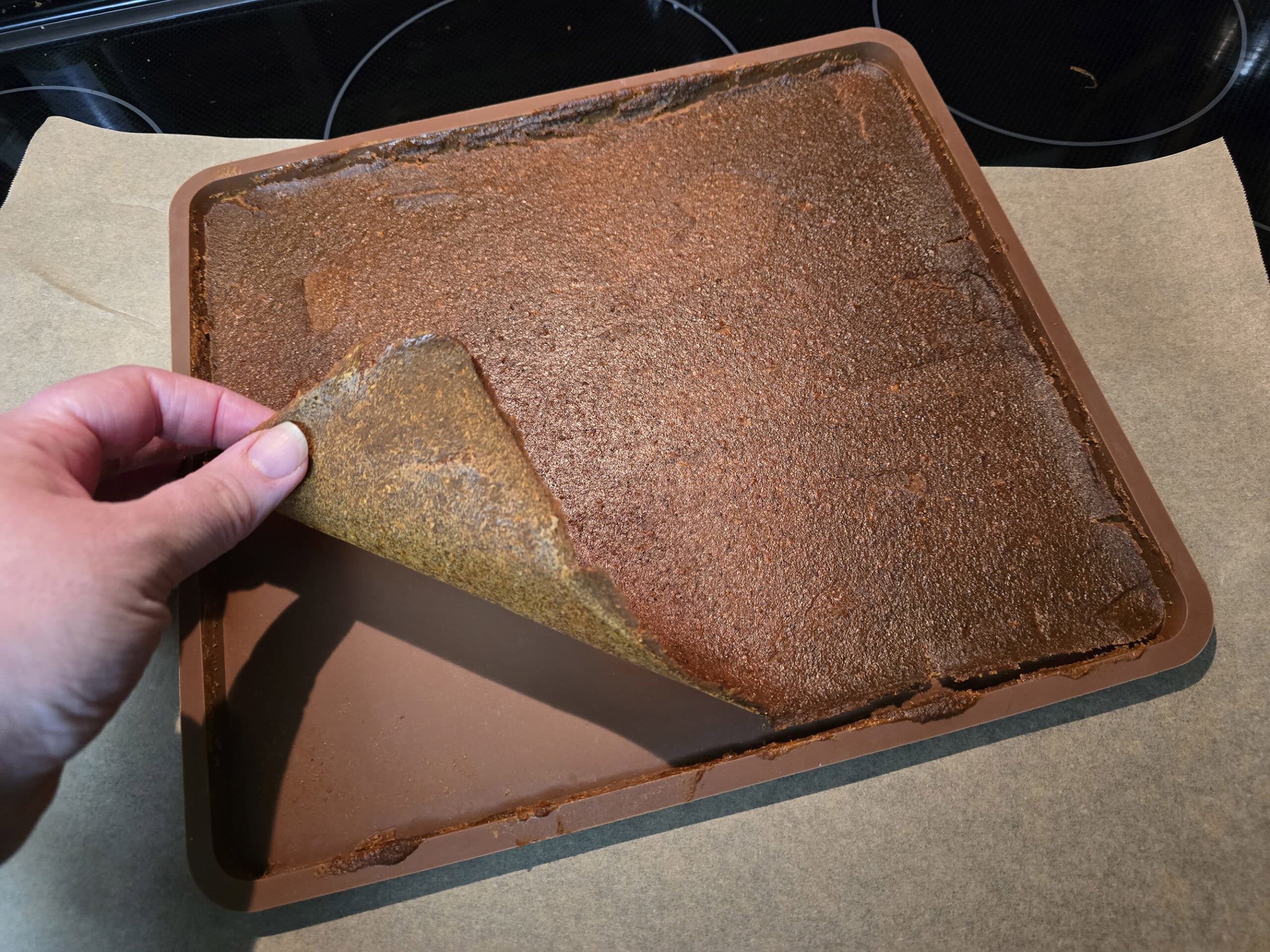 A hand pulls up a corner of pumpkin spice fruit leather being pulled up from a silicone dehydrator tray.