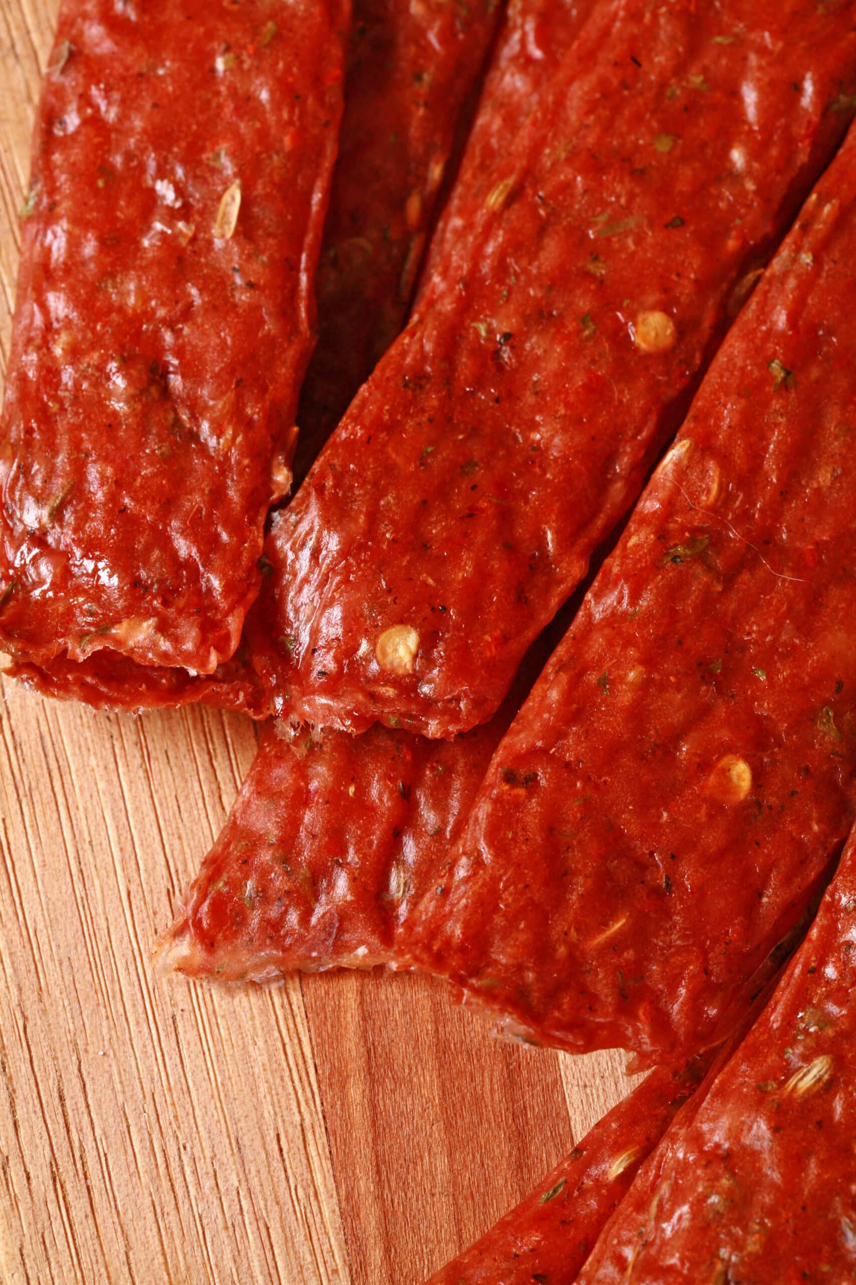 Several strips of Spicy Italian Sausage Jerky on a cutting board with fresh parsley and fennel seeds.