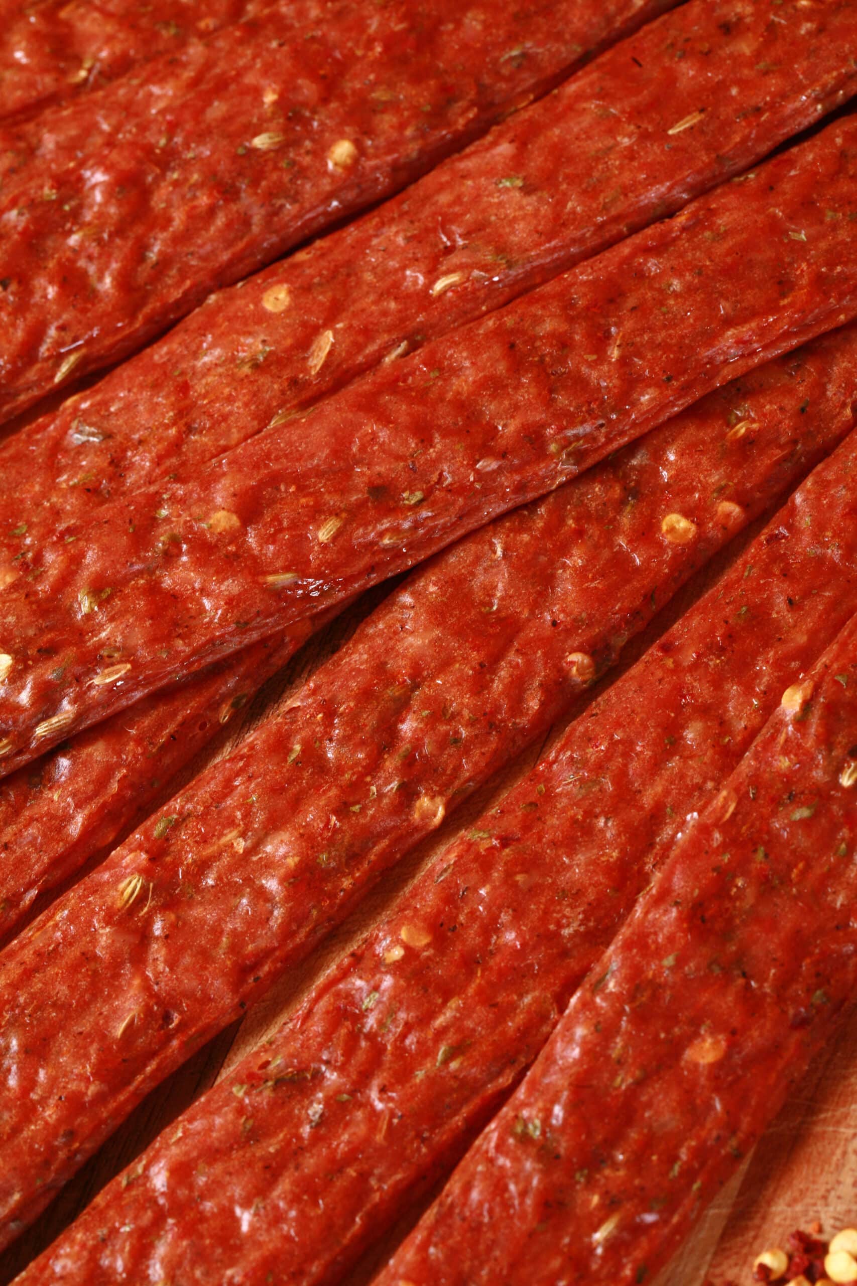 Several strips of Spicy Italian Sausage Jerky on a cutting board with fresh parsley and fennel seeds.