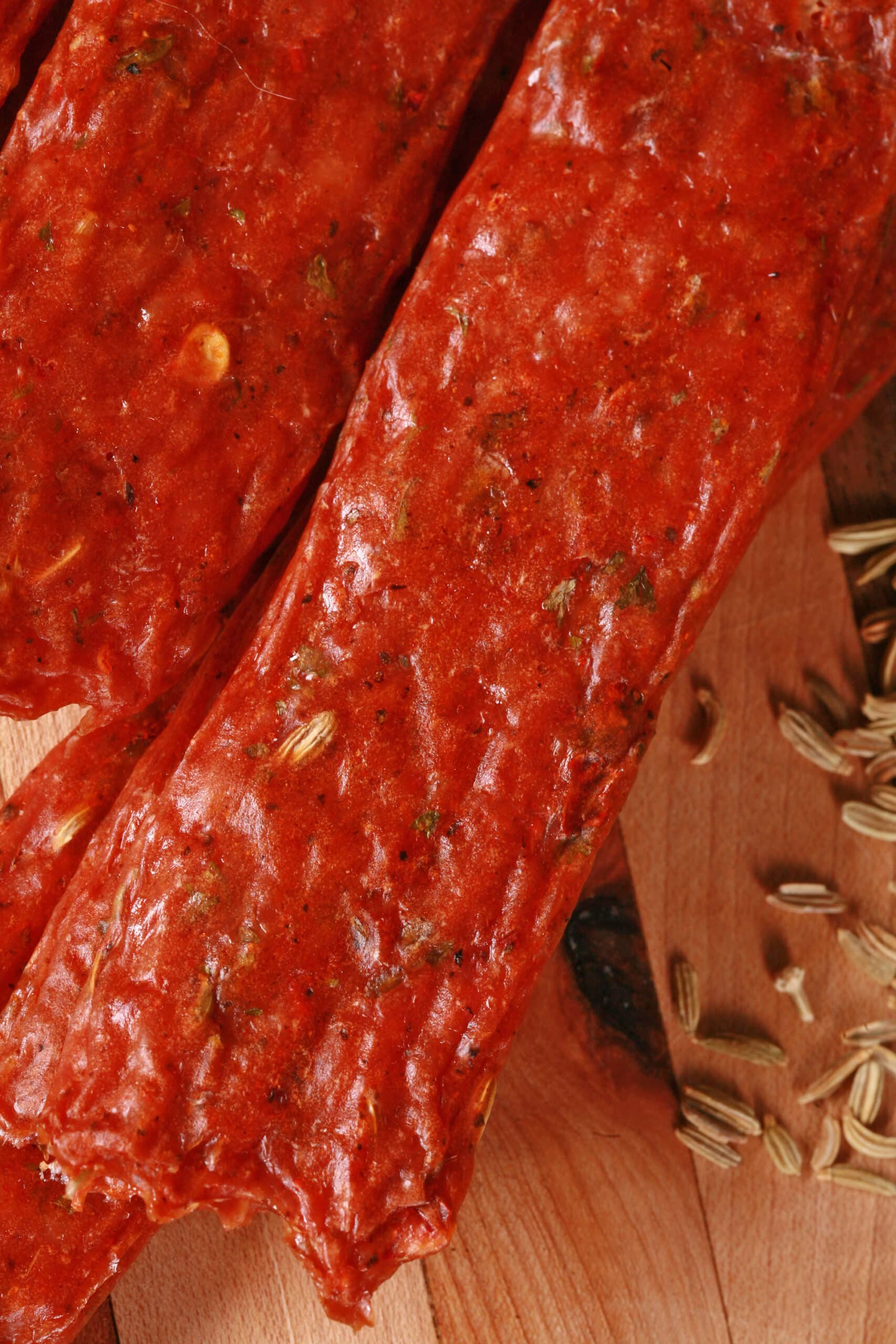 Several strips of Spicy Italian Sausage Jerky on a cutting board with fresh parsley and fennel seeds.