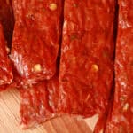 Several strips of Spicy Italian Sausage Jerky on a cutting board with fresh parsley and fennel seeds.