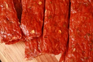 Several strips of Spicy Italian Sausage Jerky on a cutting board with fresh parsley and fennel seeds.
